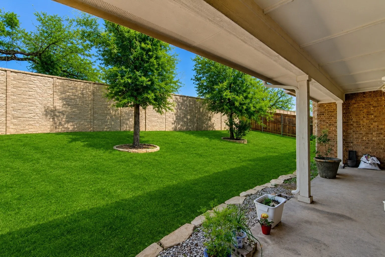 Covered patio with concrete flooring, brick exterior, and white support columns