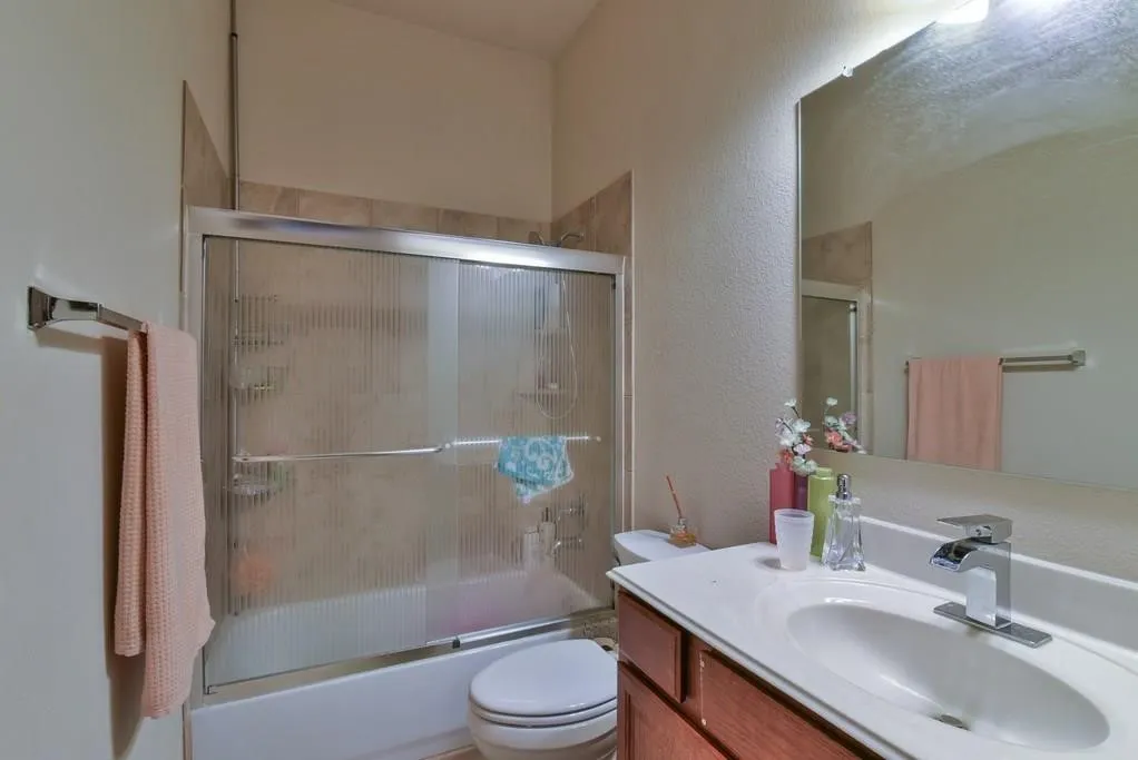 Bathroom featuring a wood-finish vanity with an integrated sink and chrome faucet, a large wall-mounted mirror, and a bathtub with a textured glass sliding door