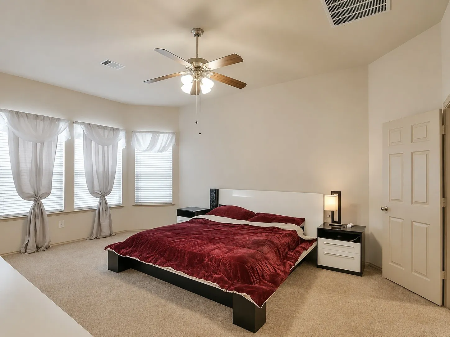 Carpeted room featuring a ceiling fan with light fixture, multiple windows with blinds, and a paneled interior door