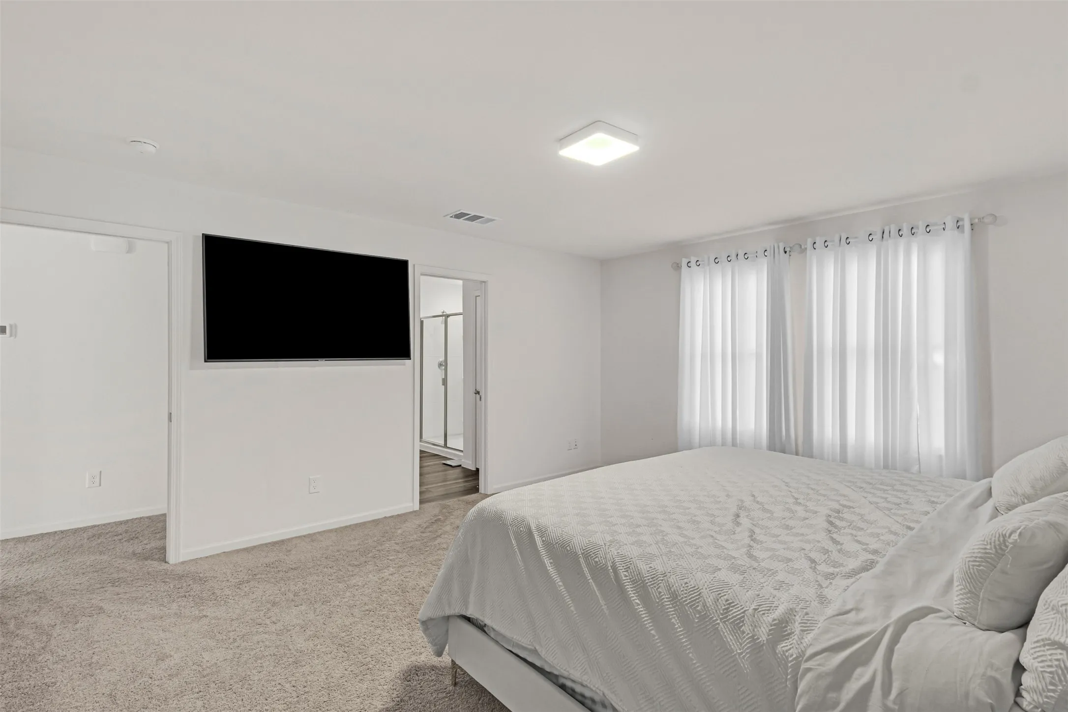 Carpeted room with white walls, dual windows featuring sheer white curtains, and a square flush-mount ceiling light