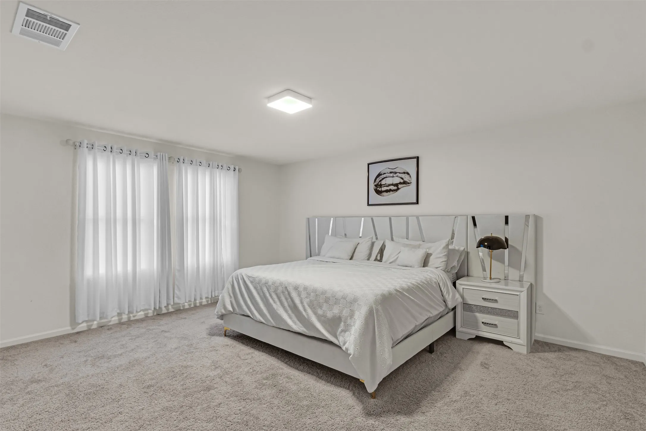 Carpeted bedroom featuring white walls and a large window with sheer white curtains