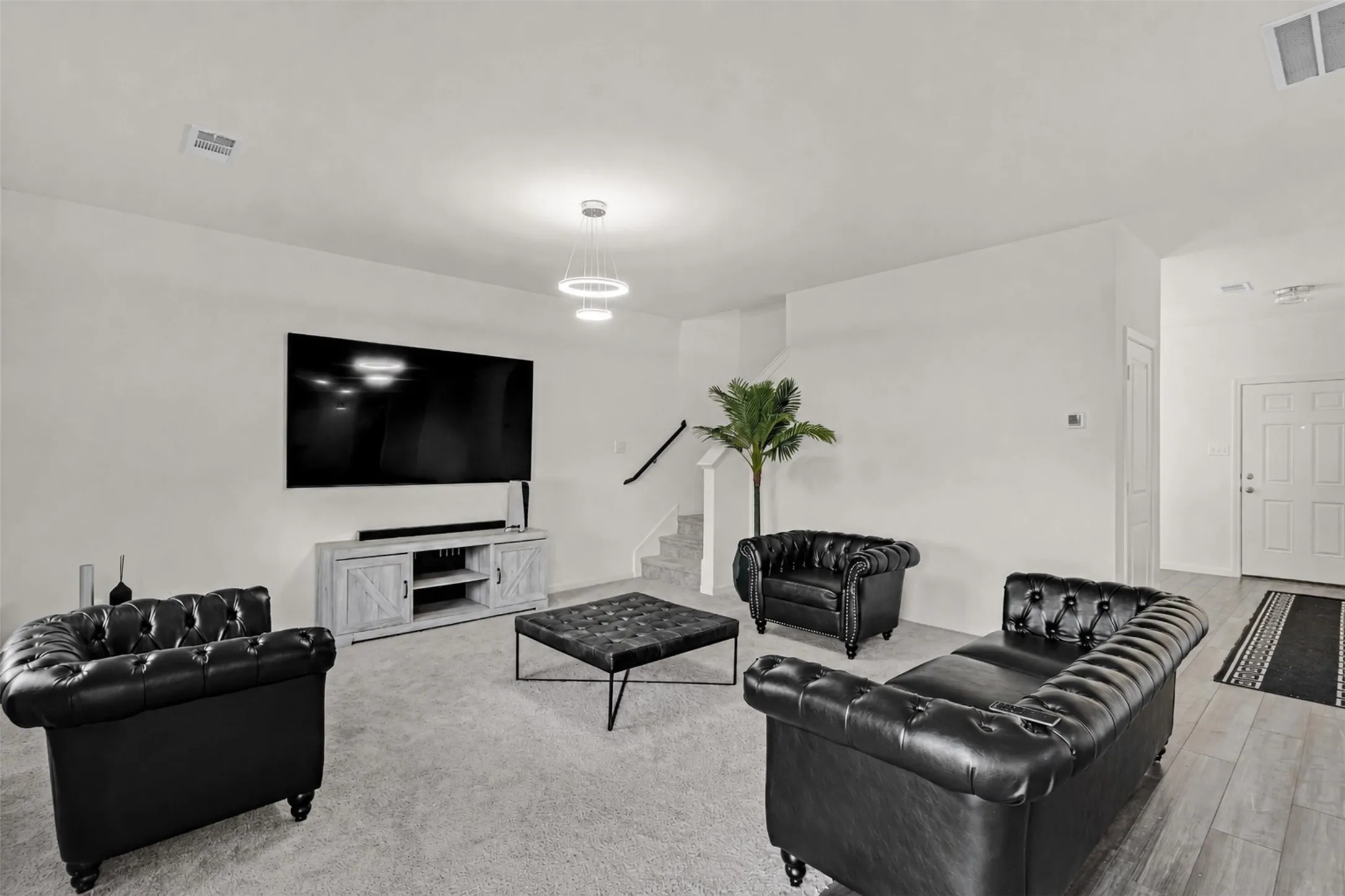 Spacious living area featuring light gray carpet flooring and contemporary pendant lighting