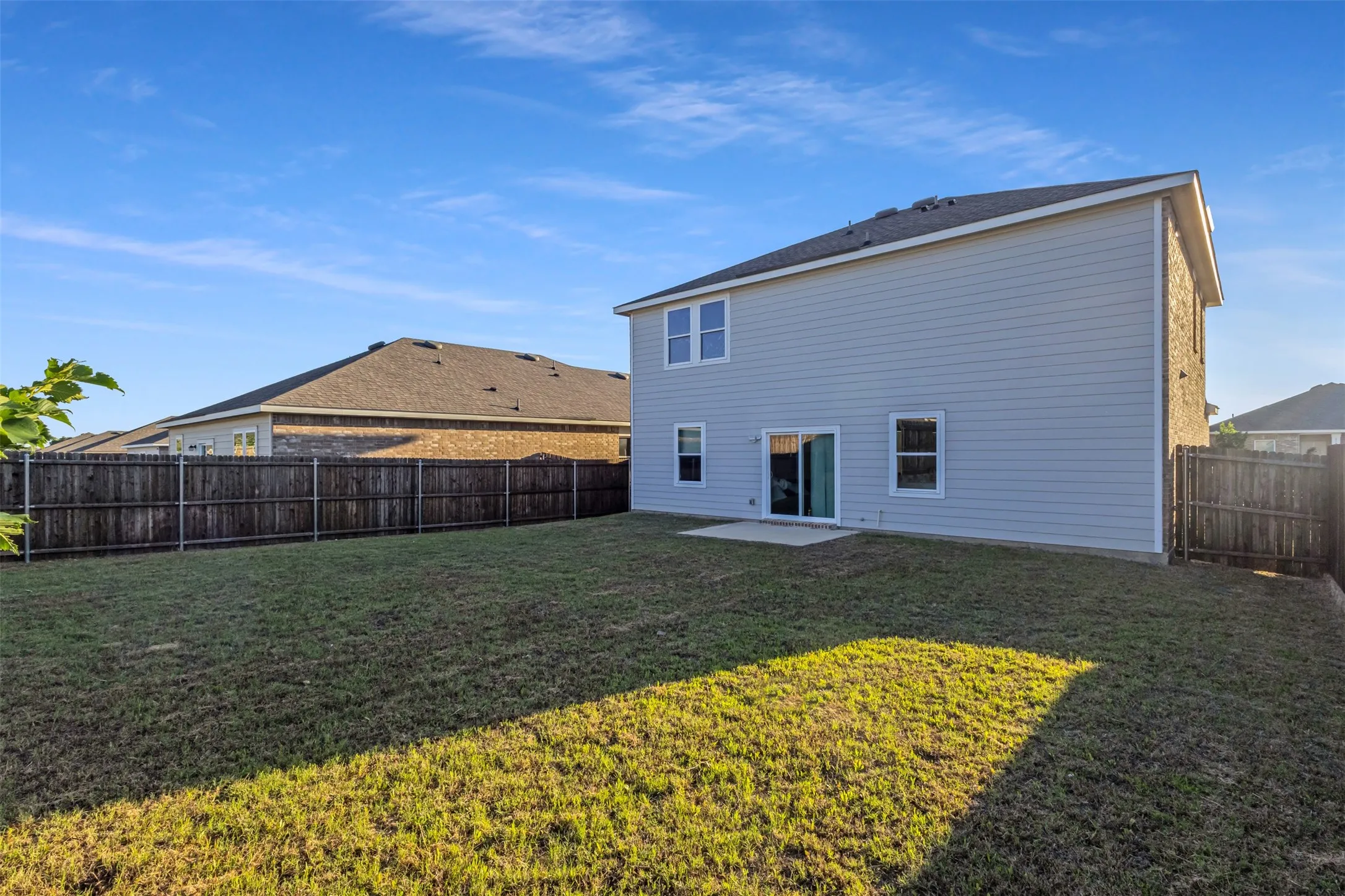 Expansive backyard featuring a manicured lawn, full privacy fencing, and a concrete patio