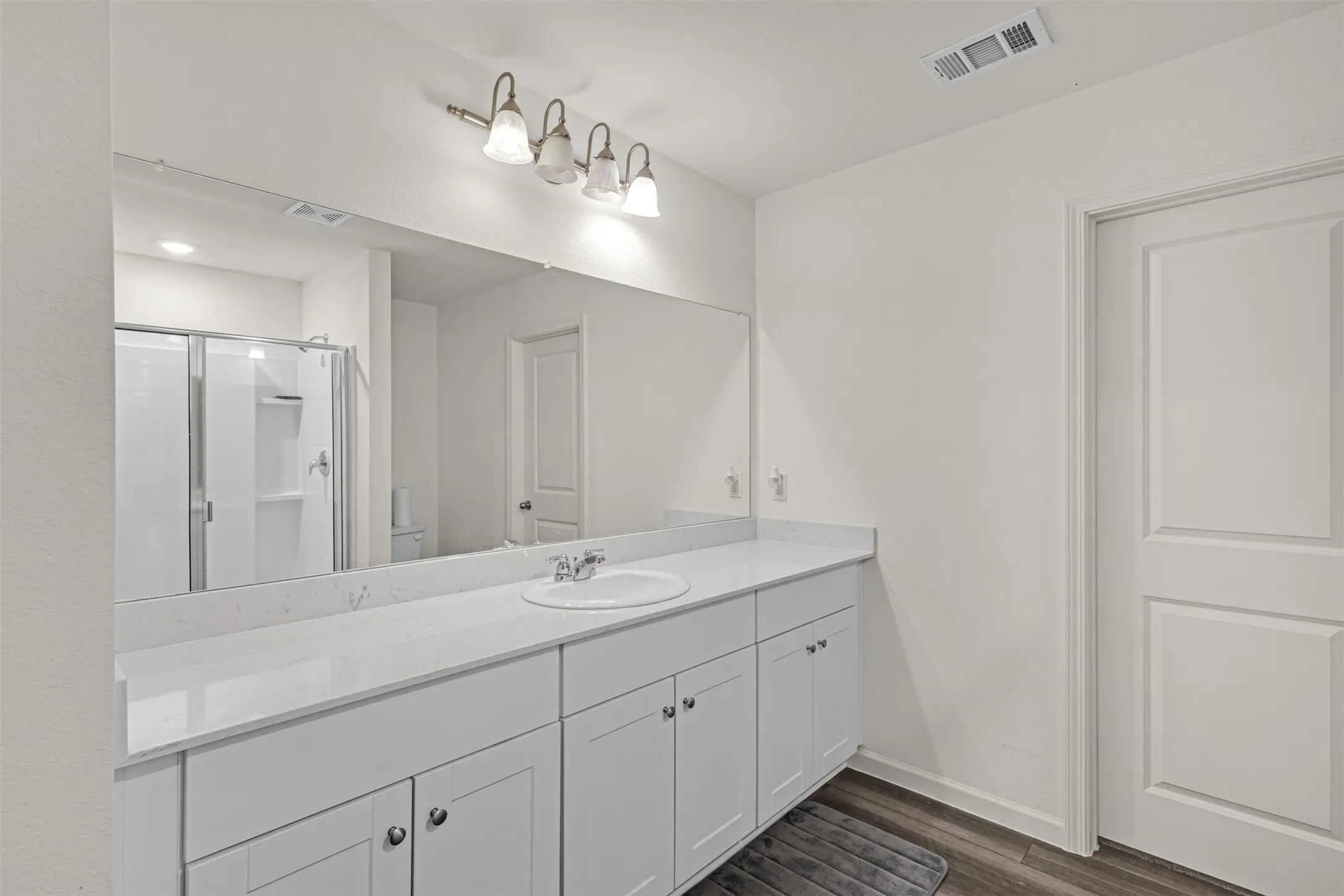 White double vanity with a single undermount sink, a large wall-mounted mirror, and a four-light vanity fixture