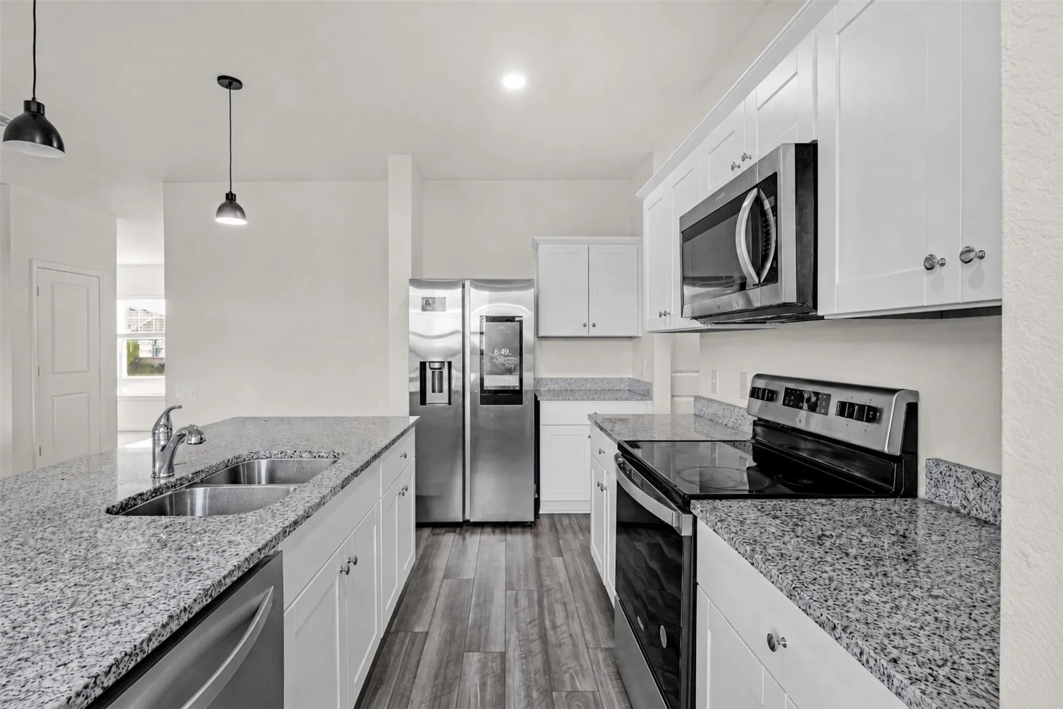 Kitchen featuring an island with double basin sink, stainless steel appliances, granite countertops, white cabinetry, and wood-finish flooring
