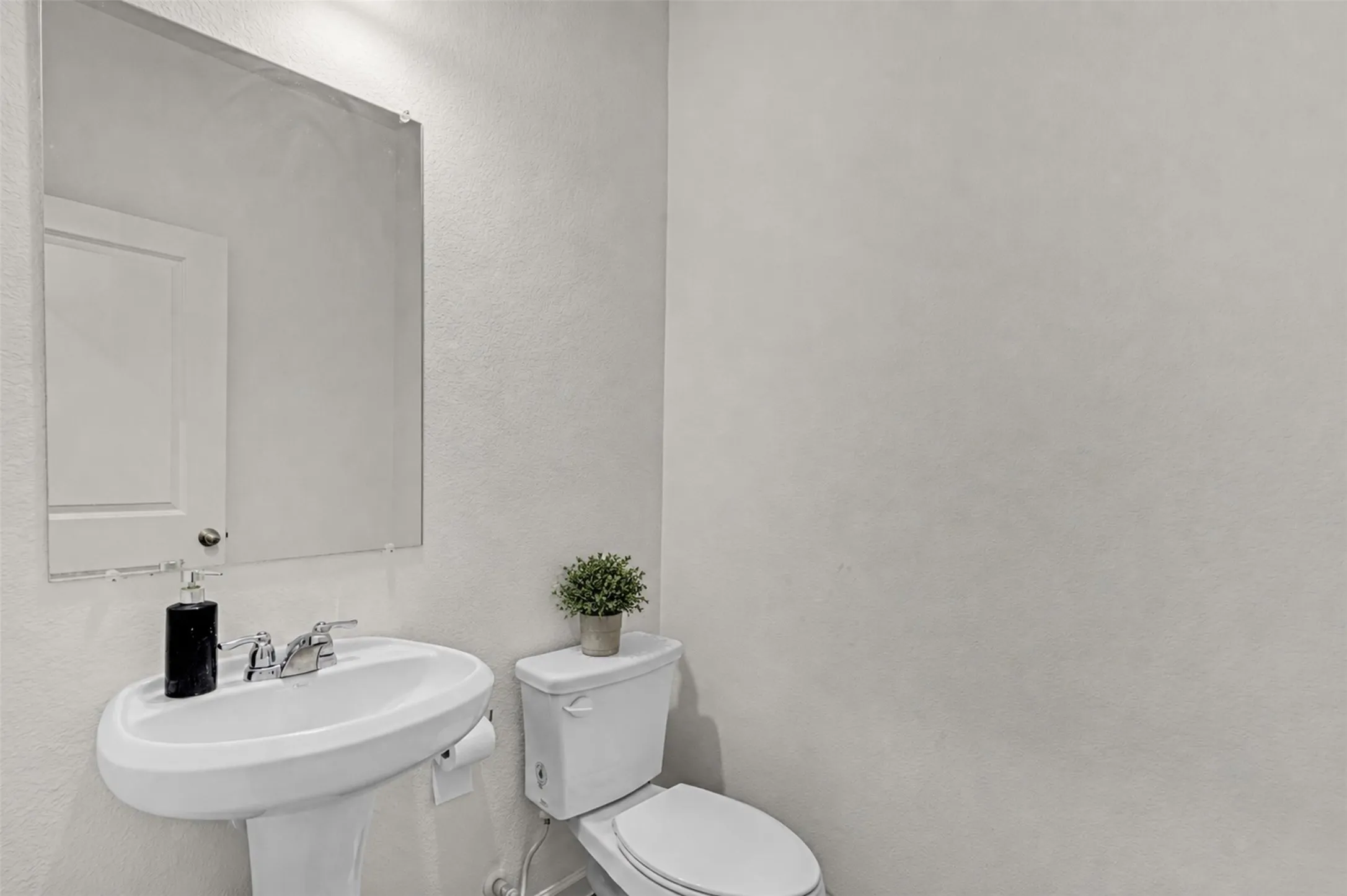 Pedestal sink with chrome faucet hardware and a frameless rectangular mirror