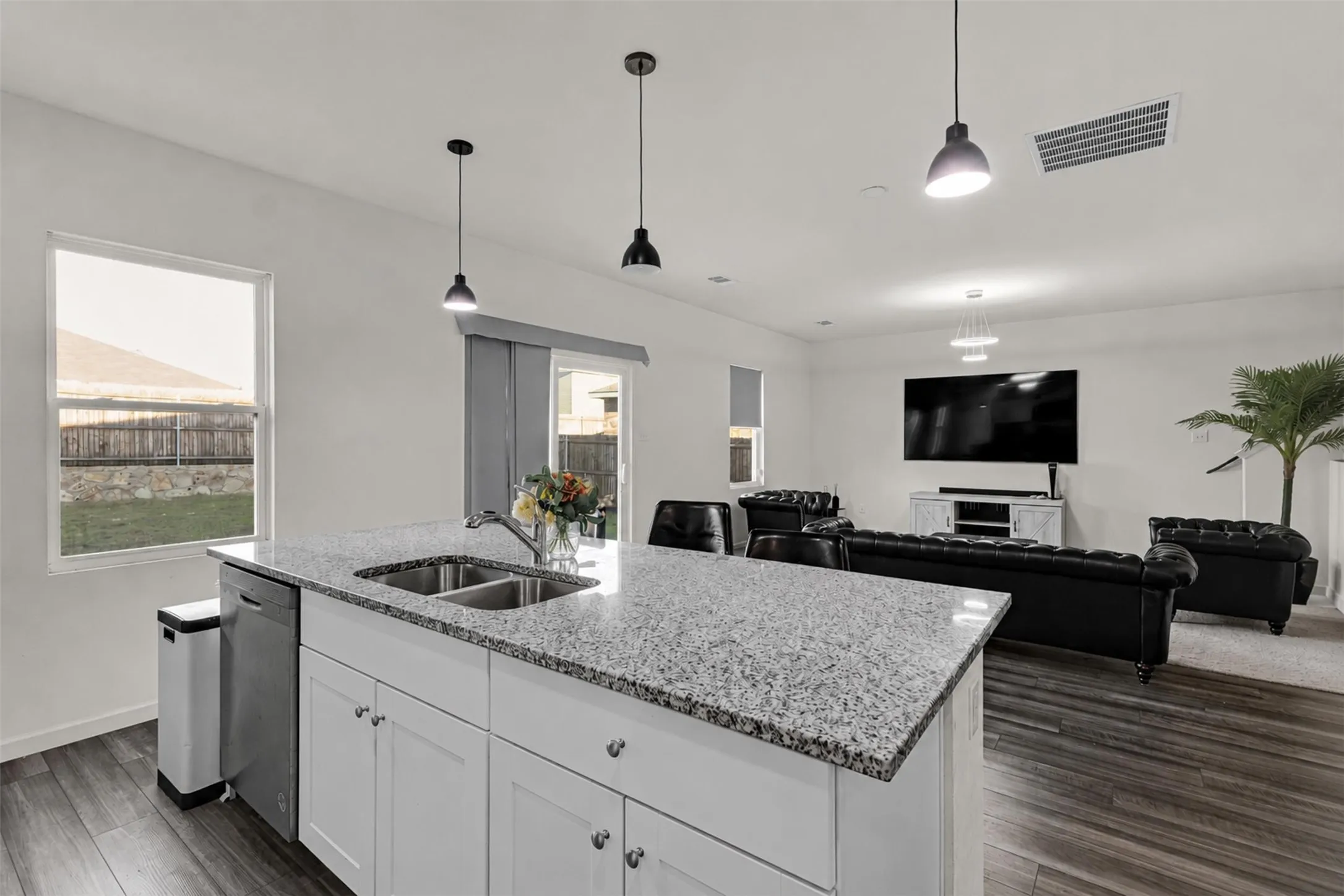 Kitchen island featuring a double-basin stainless steel sink, granite countertops, and white cabinetry with brushed nickel hardware