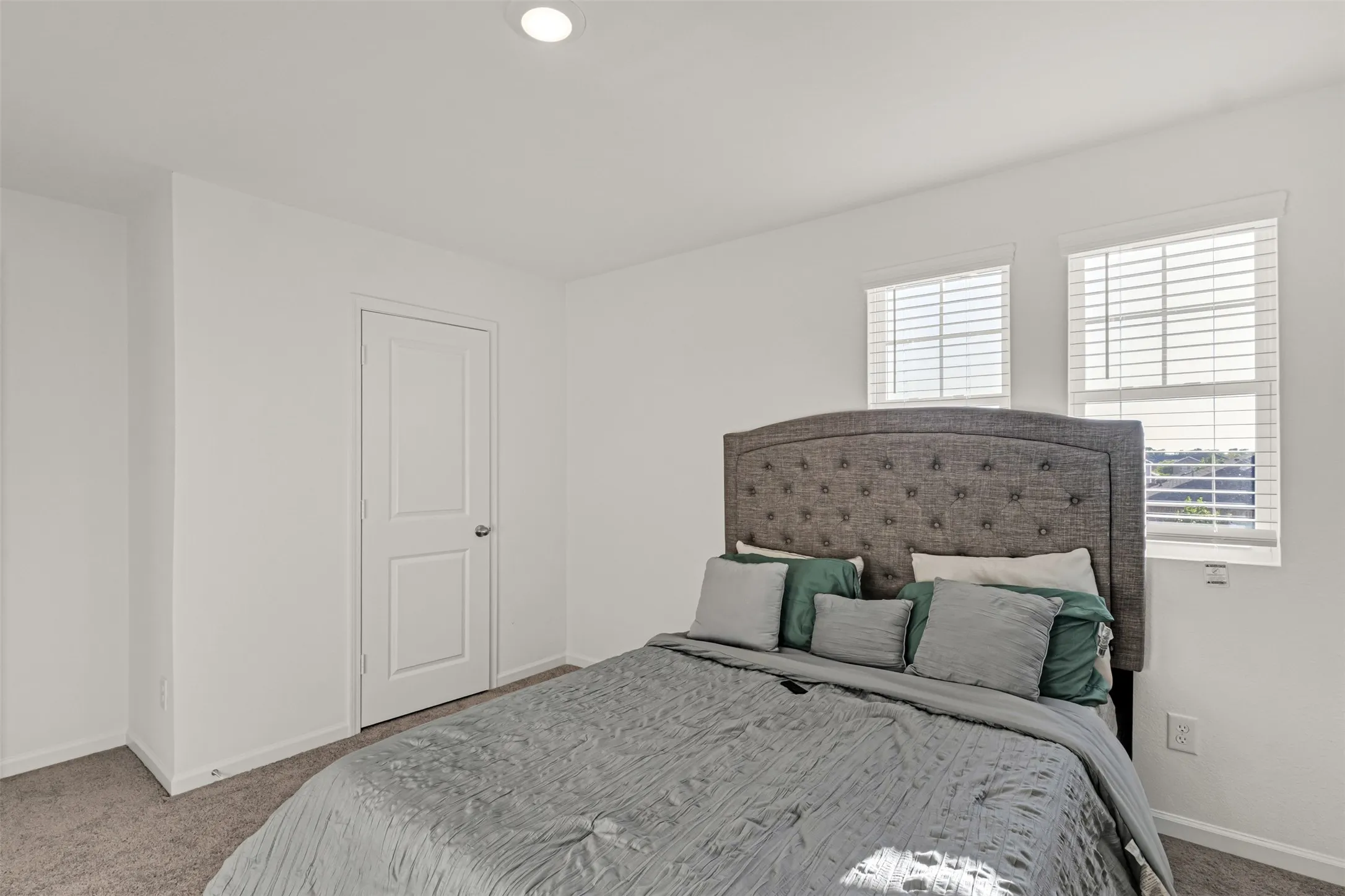 Carpeted room with white walls, two windows featuring white blinds, a paneled door with a silver knob, and recessed ceiling lighting