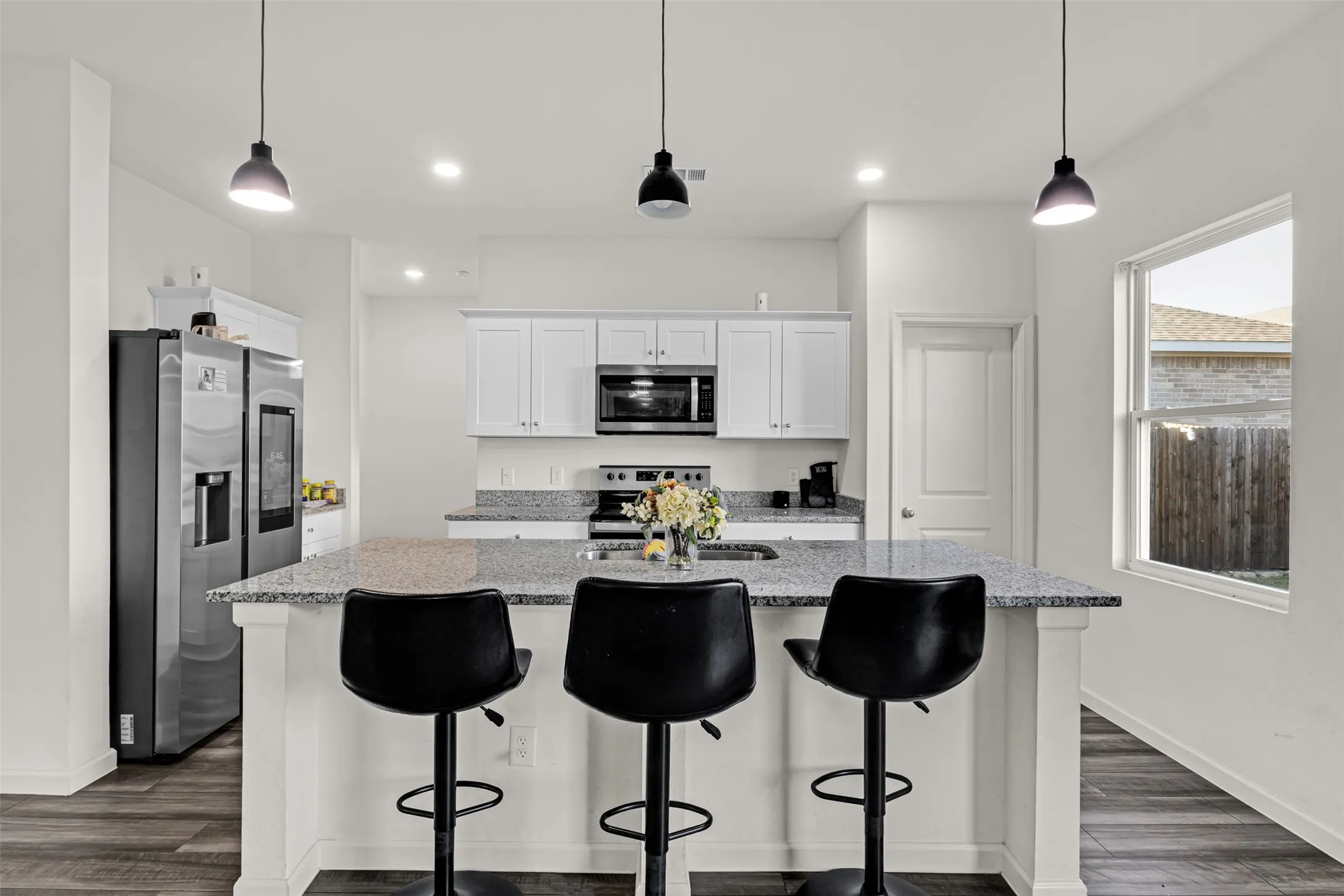Kitchen featuring an island with granite-finish countertop, white cabinetry, integrated stainless steel appliances, and wood-finish flooring