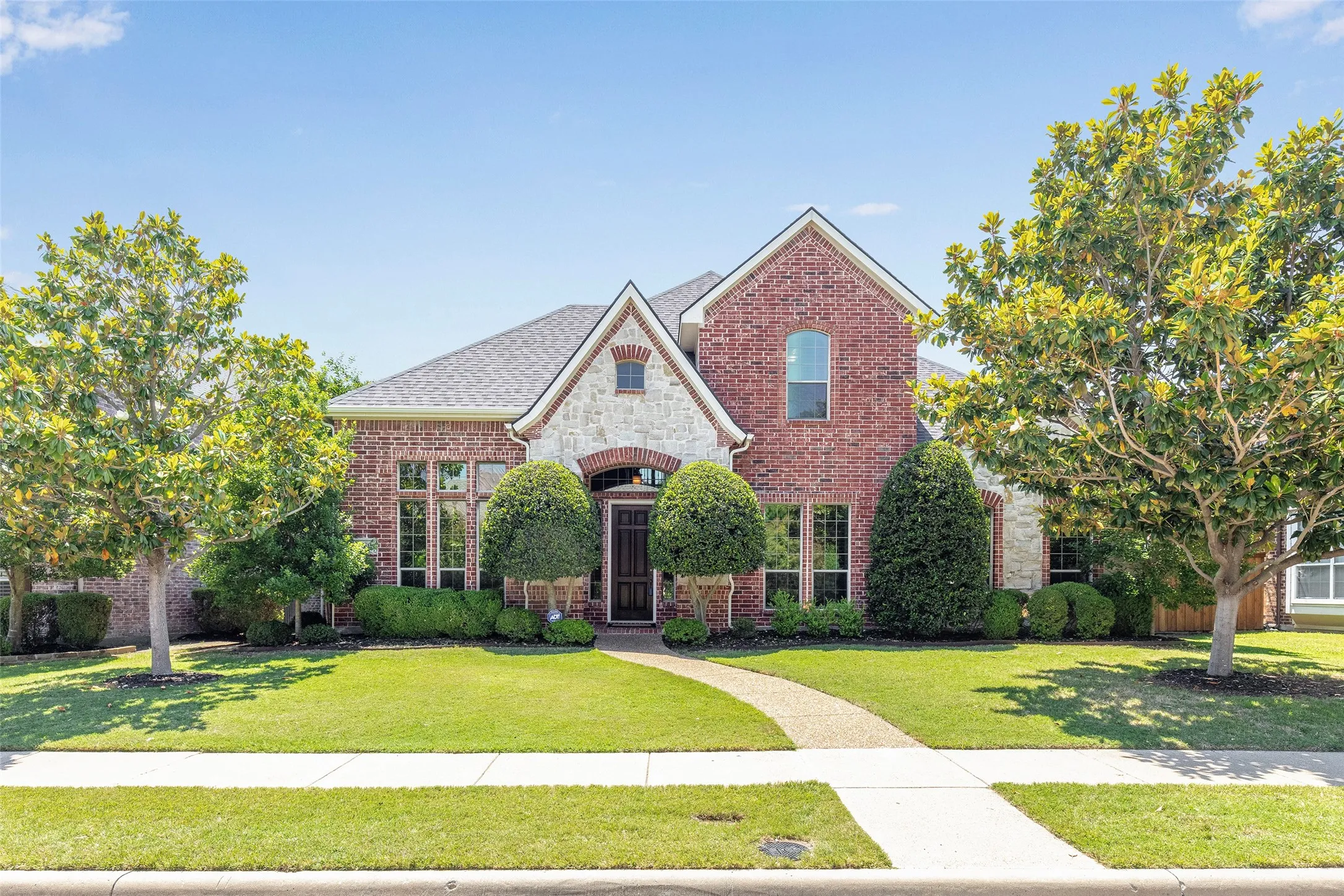 Framed by mature magnolia trees and manicured landscaping, this stately brick-and-stone elevation creates a warm first impression from the moment you arrive.