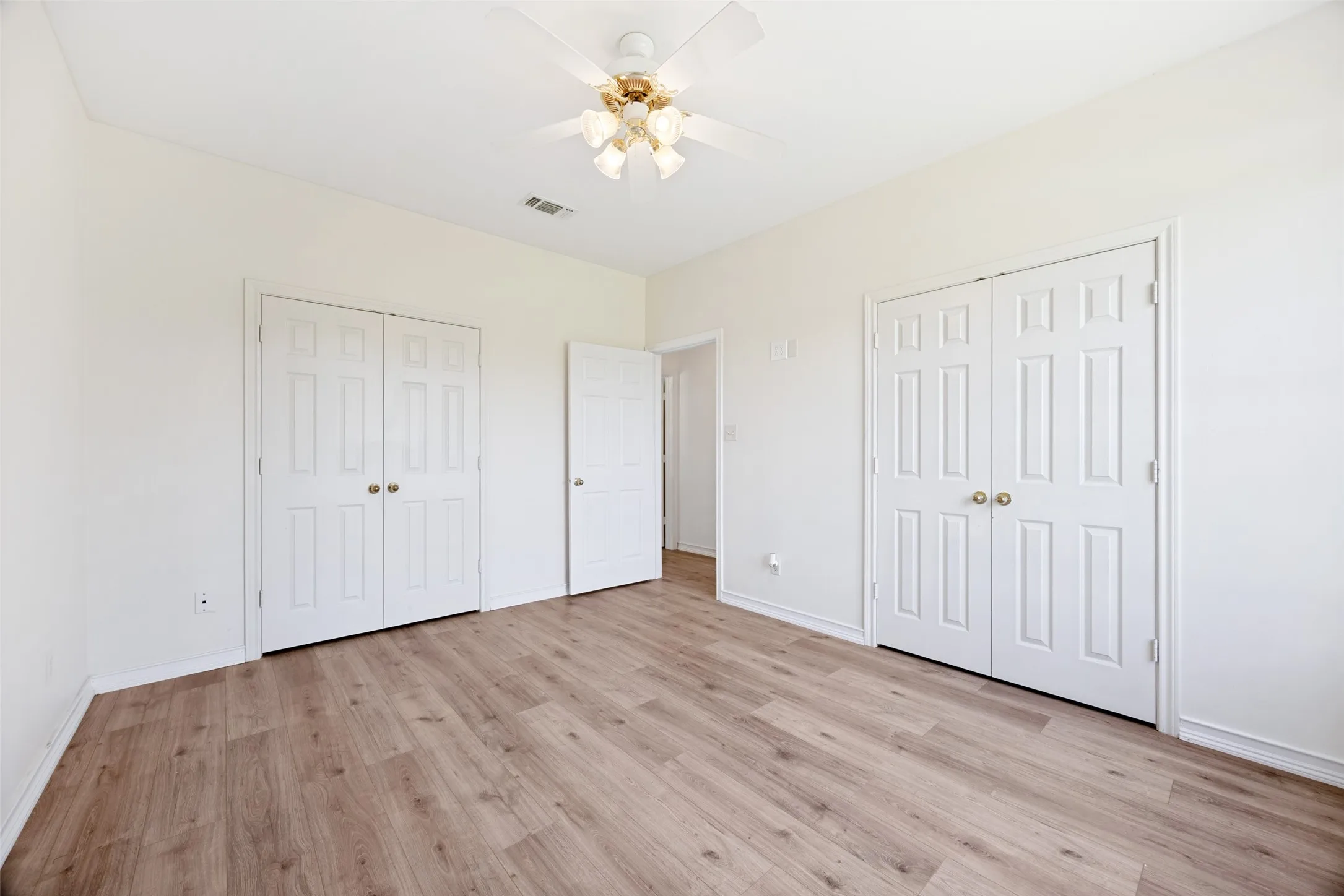 Spacious room featuring wood-finish flooring, light-toned walls, and a ceiling fan with integrated lighting