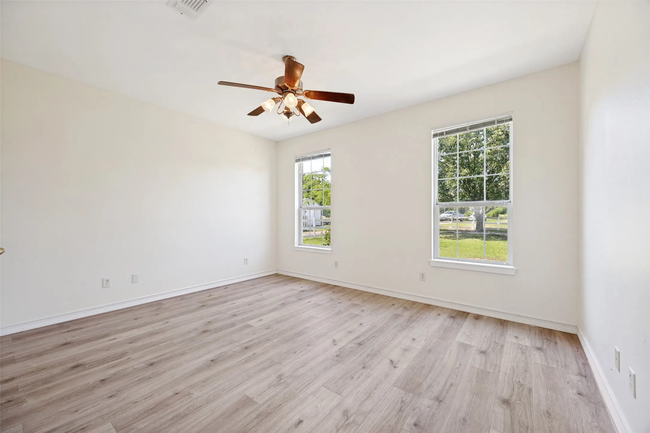 Interior room featuring wood-finish flooring, light-colored walls, and a ceiling fan with integrated lighting