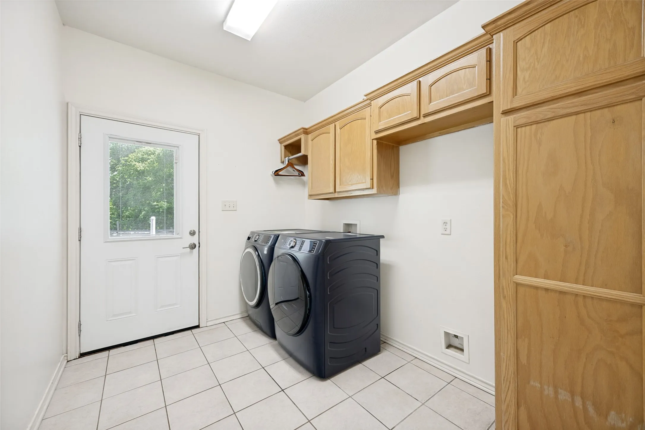 Utility space featuring wood-finish cabinetry, tile flooring, and a white exterior door with an inset window