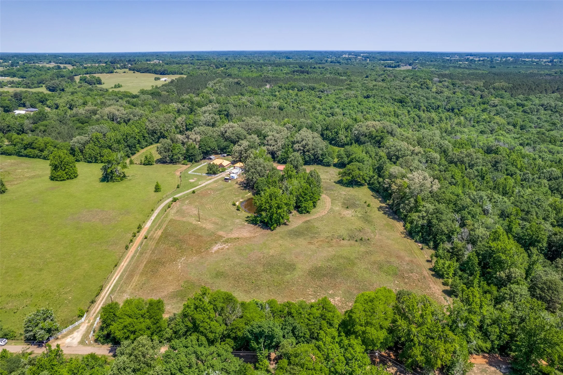 Expansive rural landscape featuring a private drive, open pastures, dense tree lines, and a visible pond