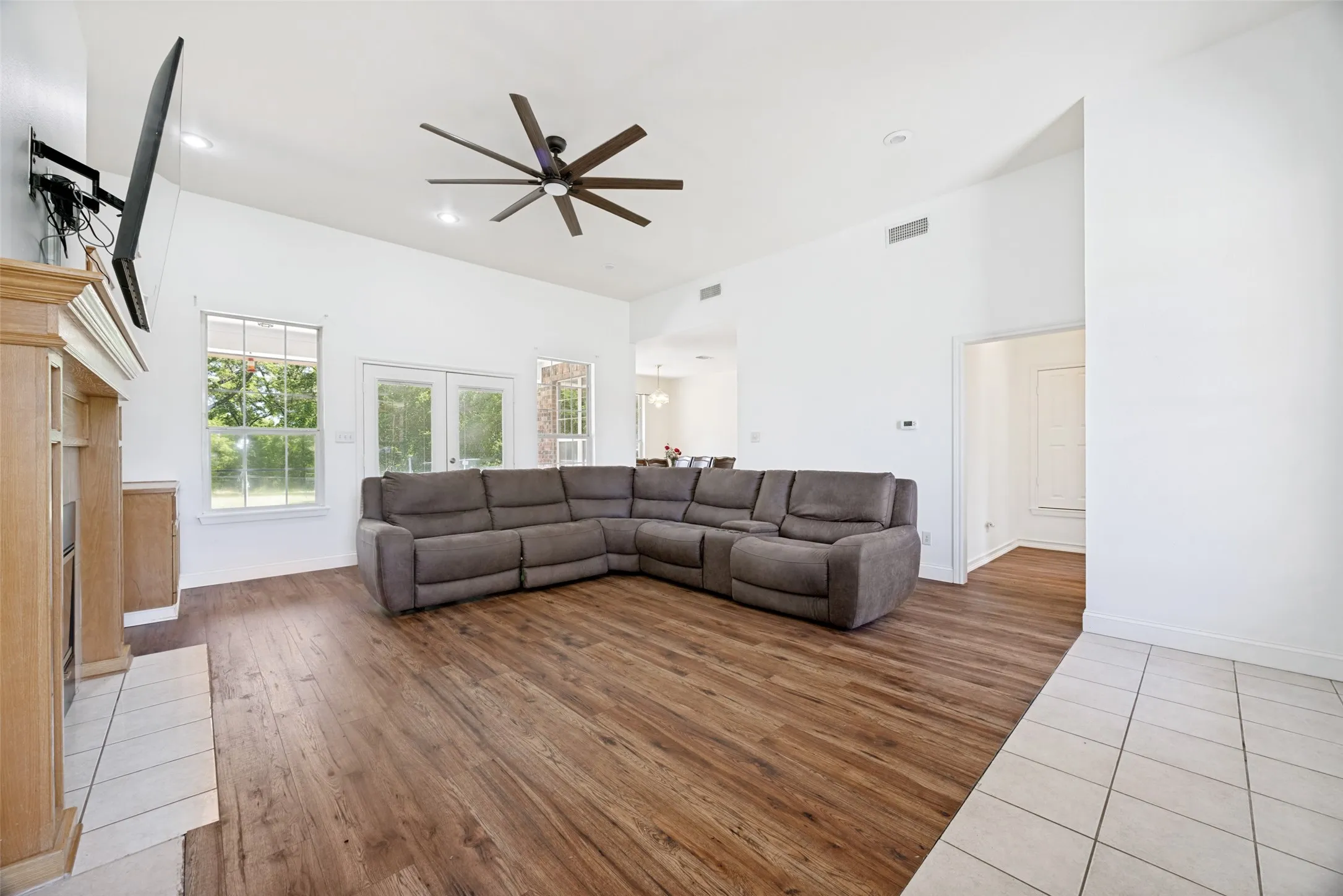 Spacious living area featuring wood-finish flooring, a fireplace with a wood mantle, and a contemporary ceiling fan