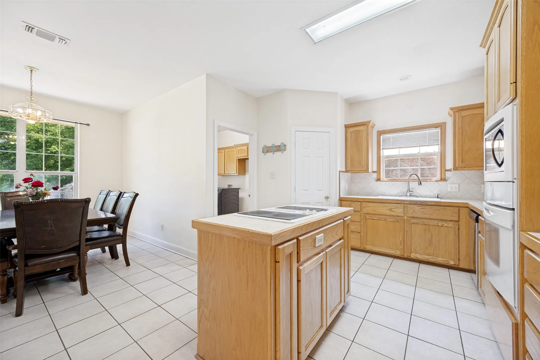 Kitchen with light wood cabinetry, white tiled flooring, and a central island with an integrated cooktop