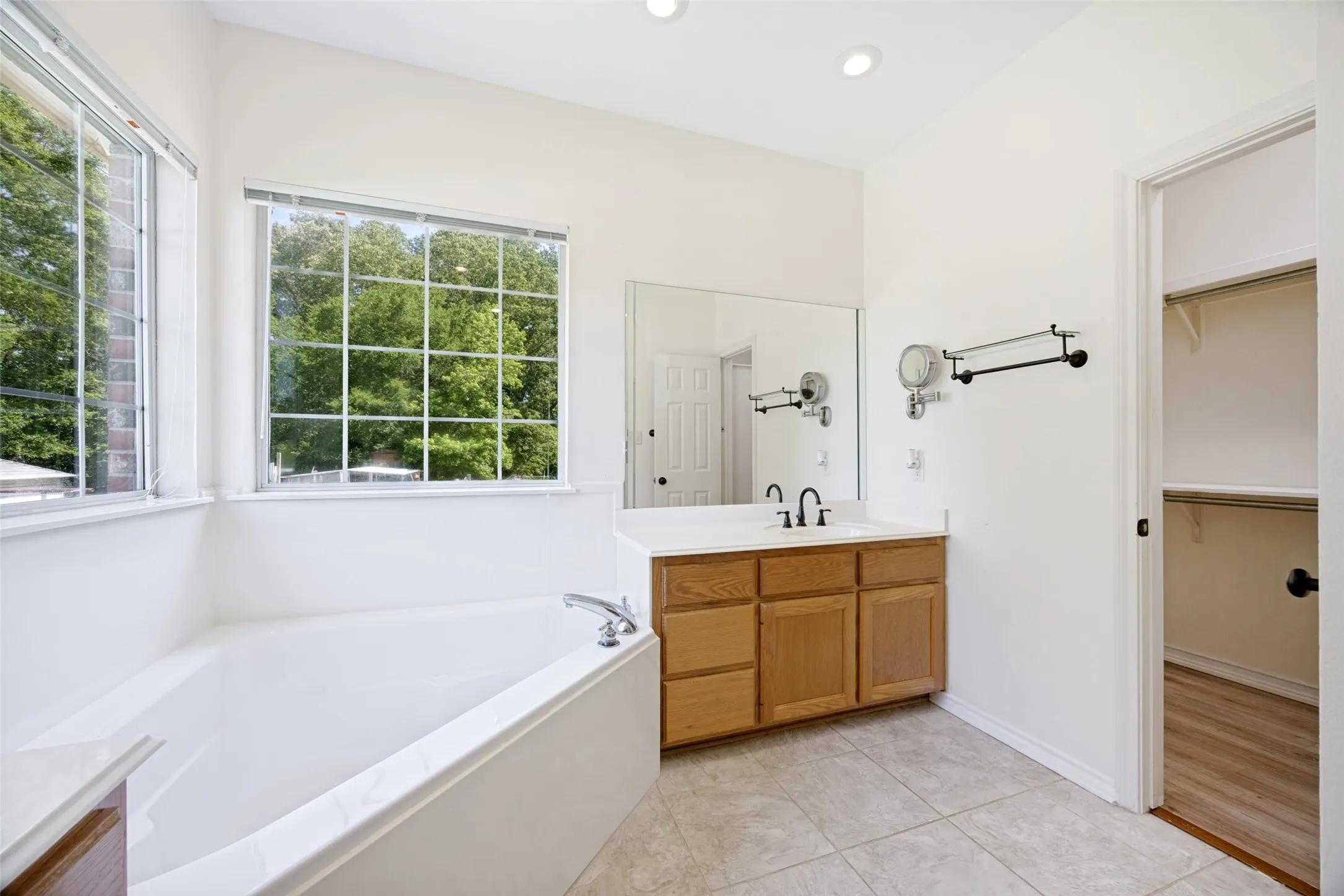 Bathroom featuring a built-in tub, dual windows with grids, recessed lighting, a wood-finish vanity with a built-in sink, and a mirrored wall