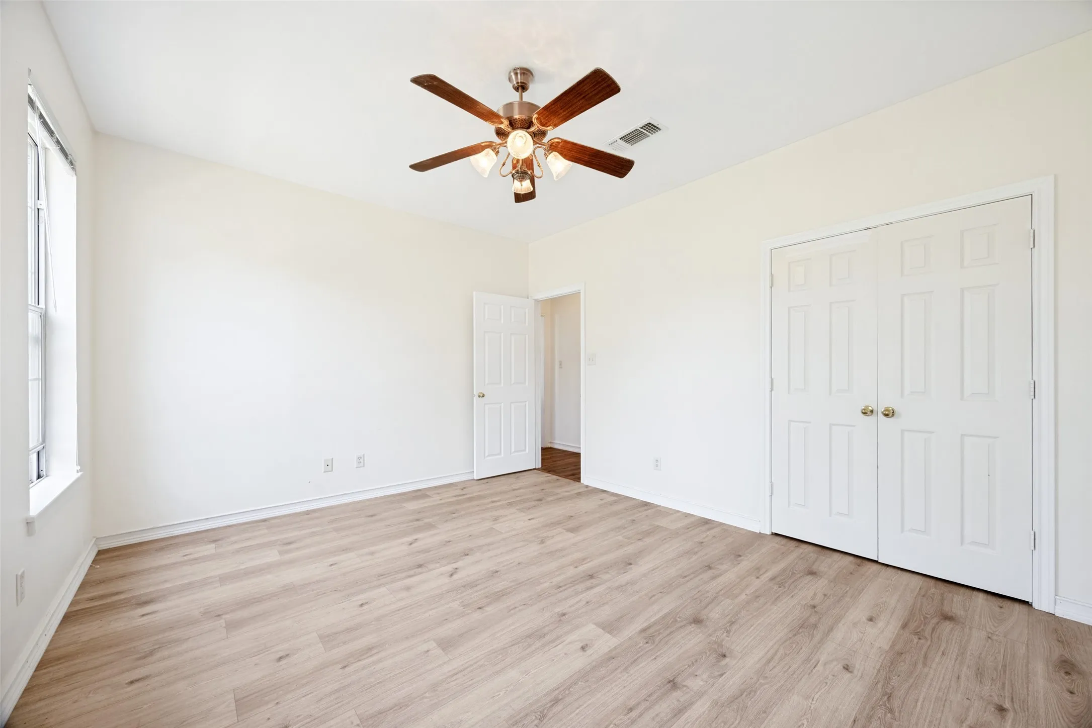Spacious interior room featuring wood-finish flooring, a ceiling fan with integrated lighting, and white walls