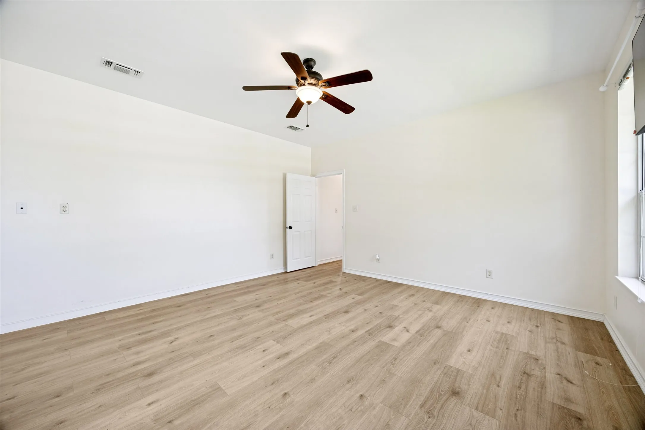 Spacious room featuring wood-finish flooring, white walls, and a ceiling fan with integrated lighting