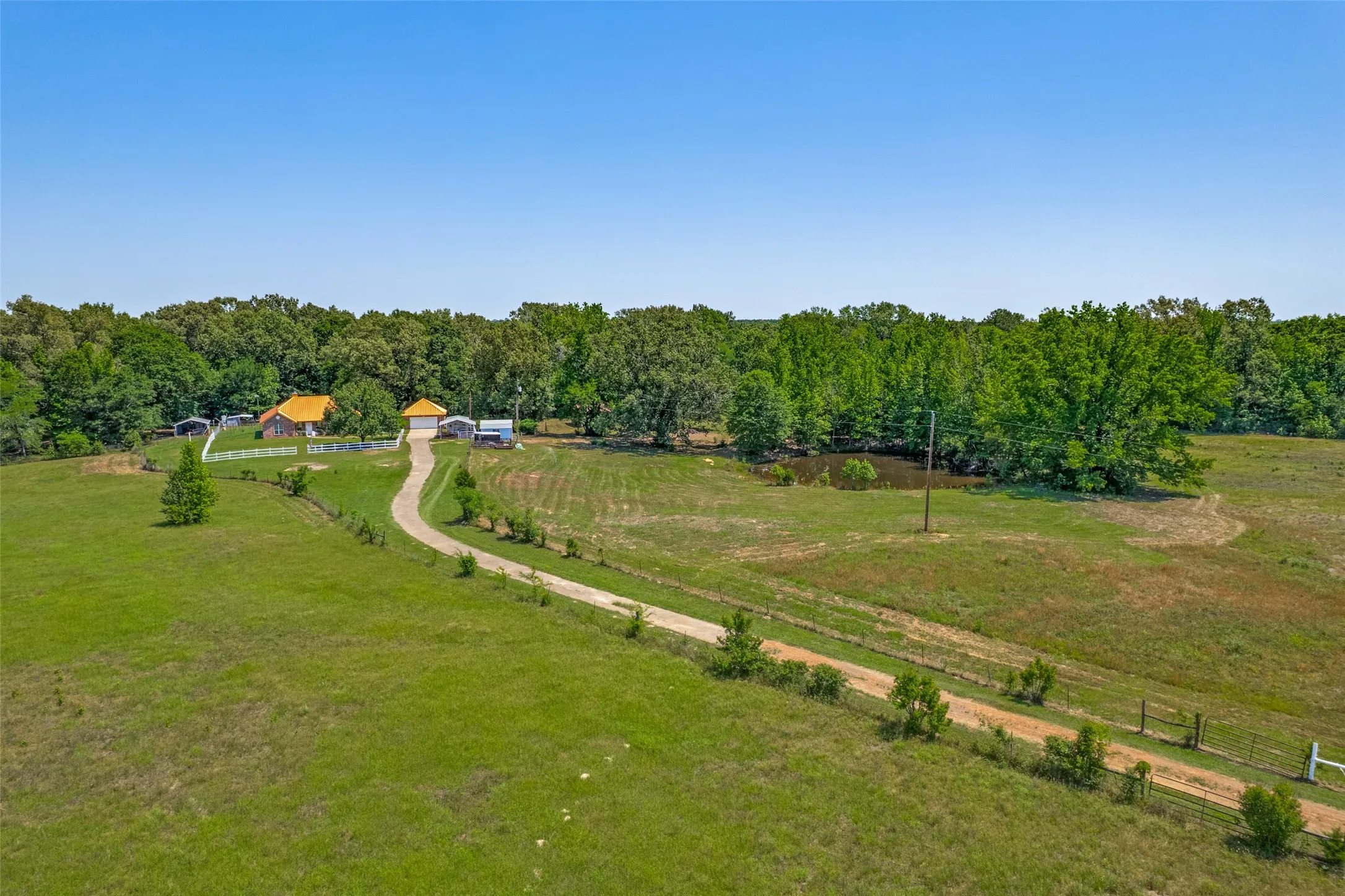 Expansive property featuring a winding driveway, a single-story residence with a prominent roof, multiple outbuildings, a pond, and mature tree lines
