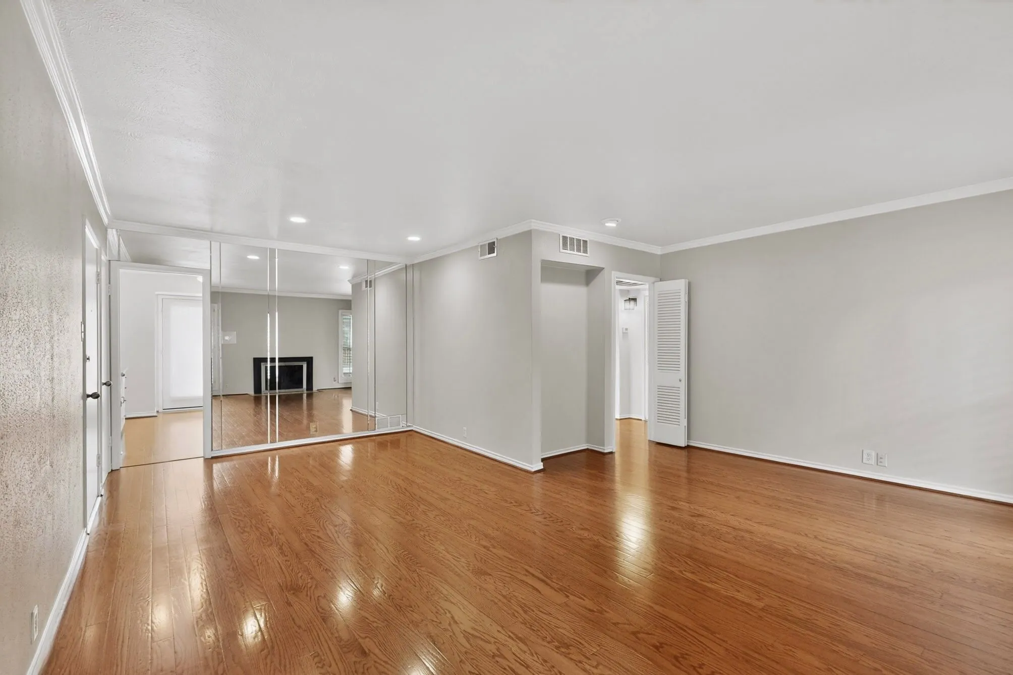 Spacious interior featuring wood-finish flooring, light grey painted walls, white crown molding, recessed lighting, and a mirrored accent wall