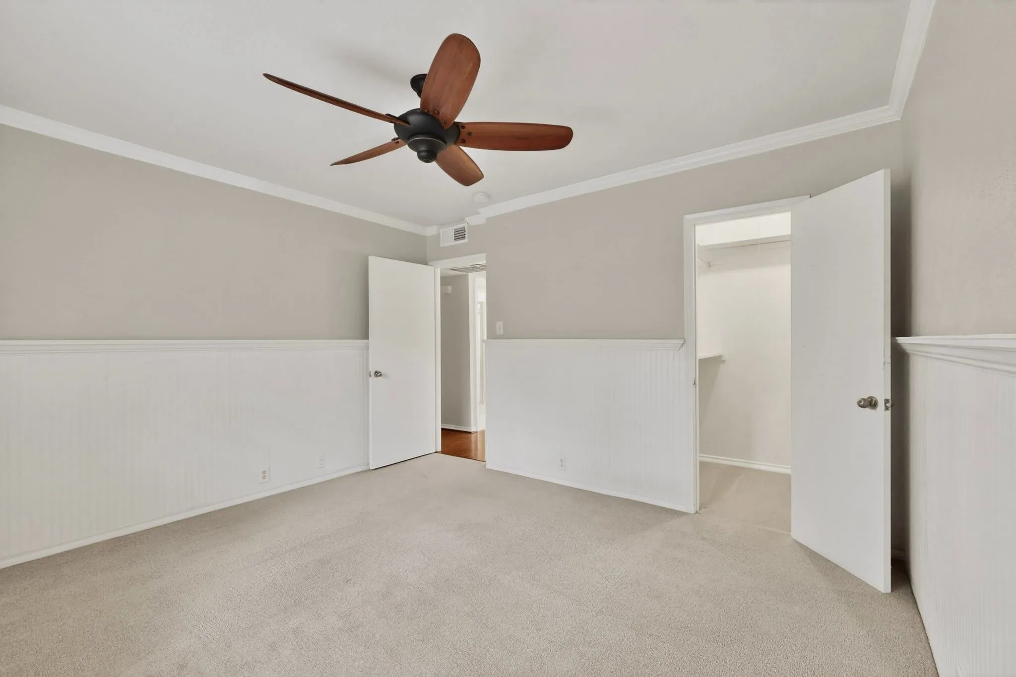 Carpeted room featuring wainscoting, crown molding, and a ceiling fan with wood-finish blades