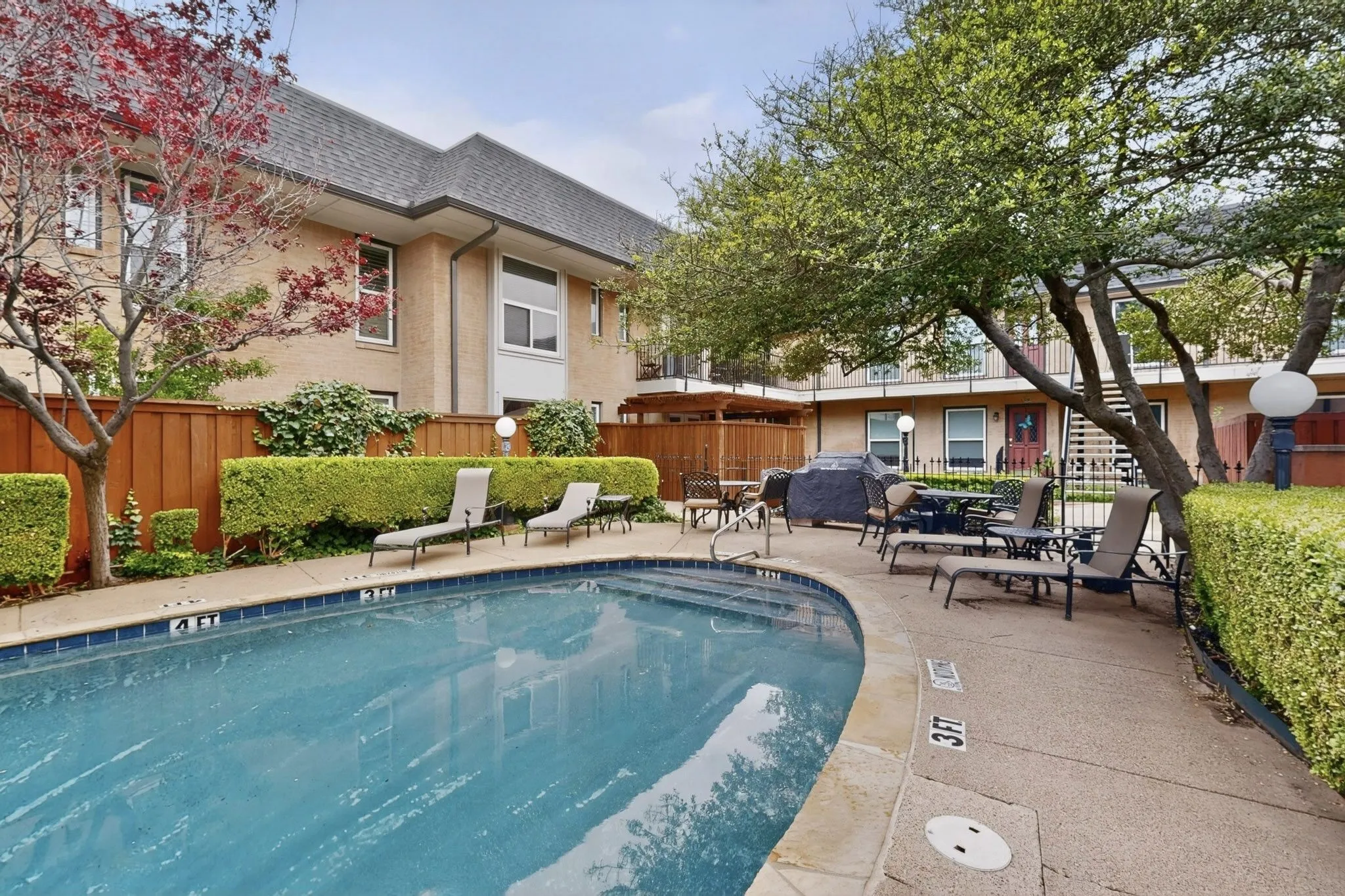 Curved swimming pool with blue tile coping, surrounded by a concrete deck