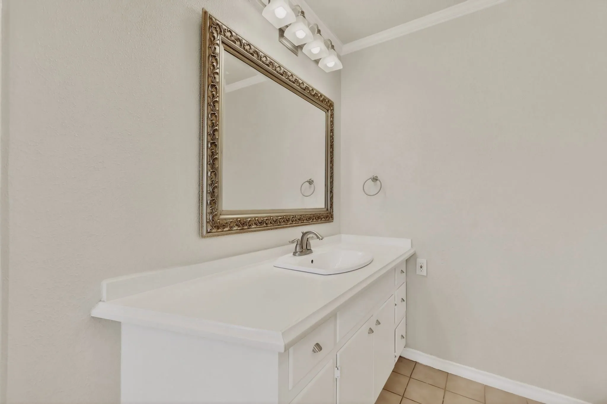 Vanity featuring an ornate gold-framed mirror, four-bulb vanity lighting, an integrated sink, a brushed nickel faucet, and a white countertop