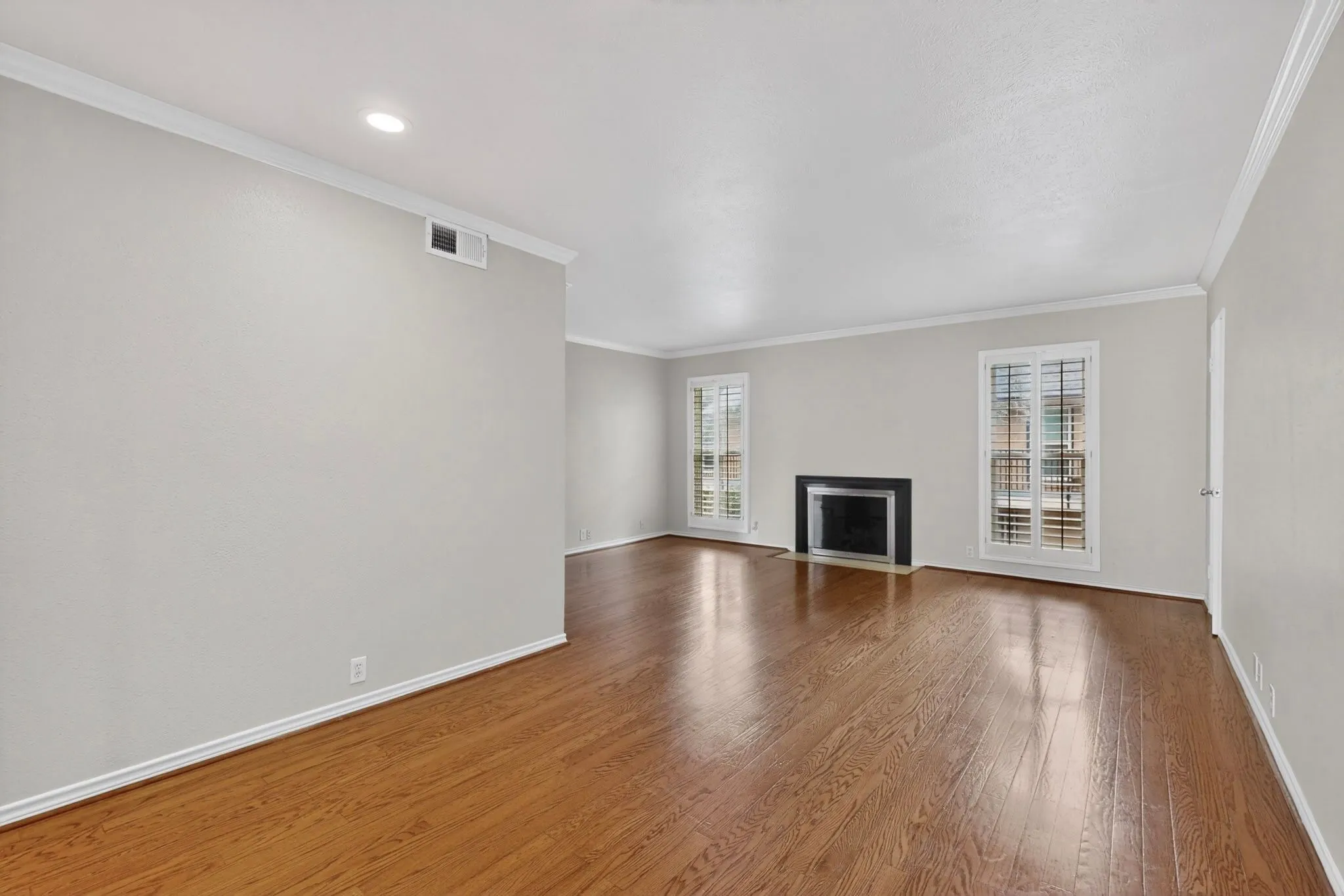 Spacious interior featuring wood-finish flooring, a contemporary fireplace with a dark surround, dual windows with plantation shutters, recessed lighting, and crown molding