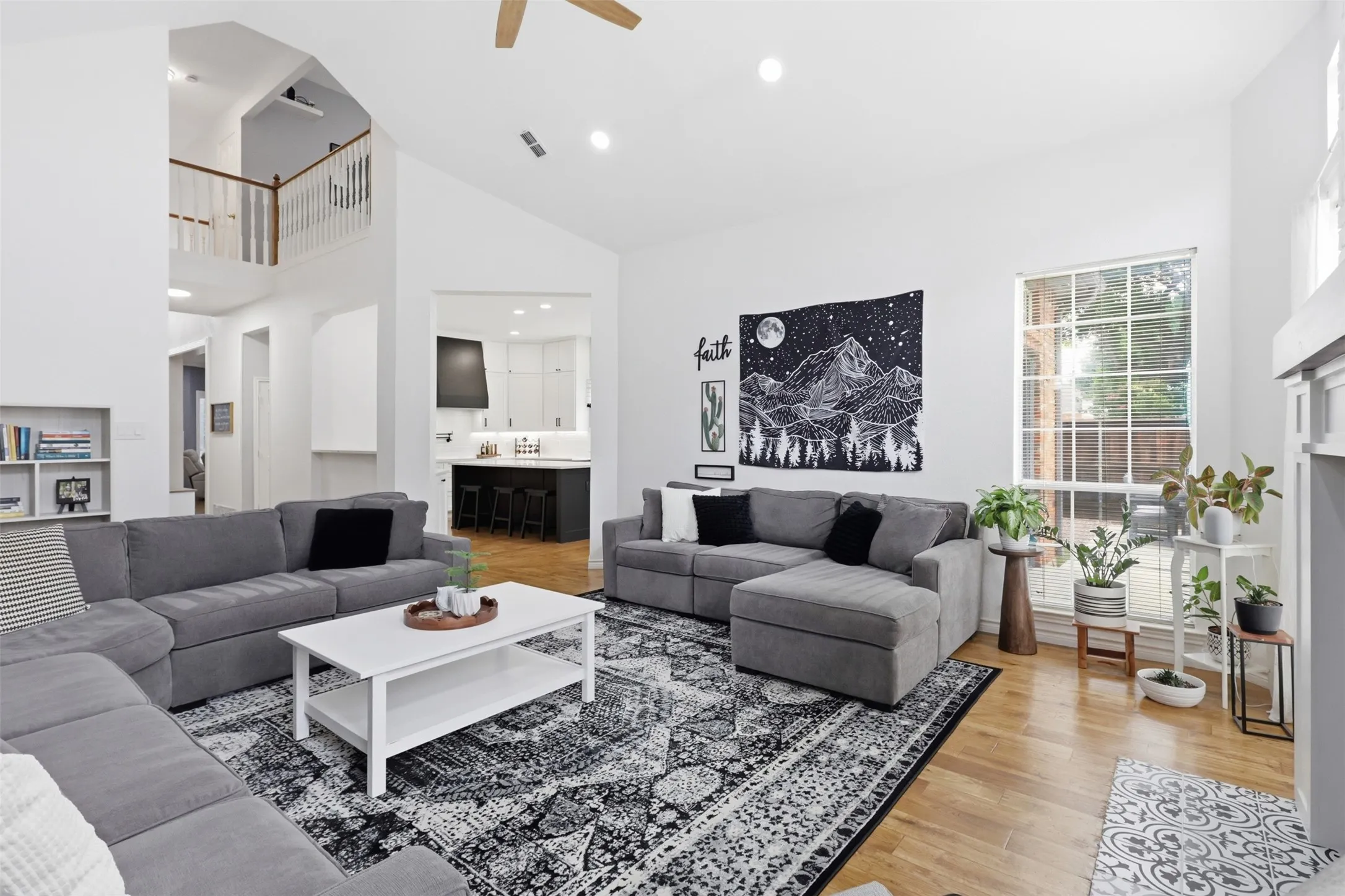 Vaulted ceilings enhance this living space featuring wood-finish flooring, a contemporary ceiling fan, and a prominent window