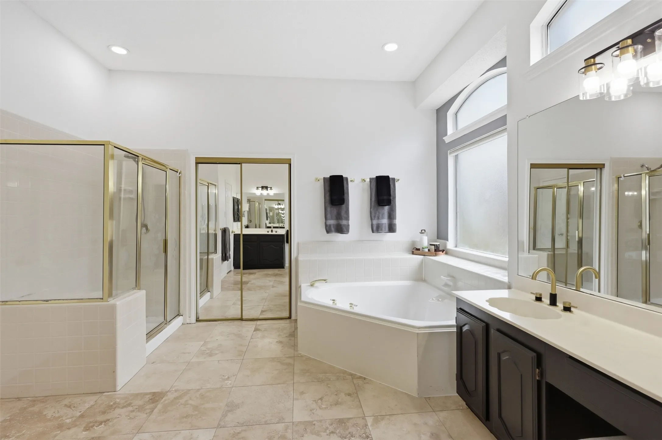 Expansive bathroom featuring a corner jetted soaking tub, separate shower with a gold-finish frame, and dual vanity with gold-finish fixtures