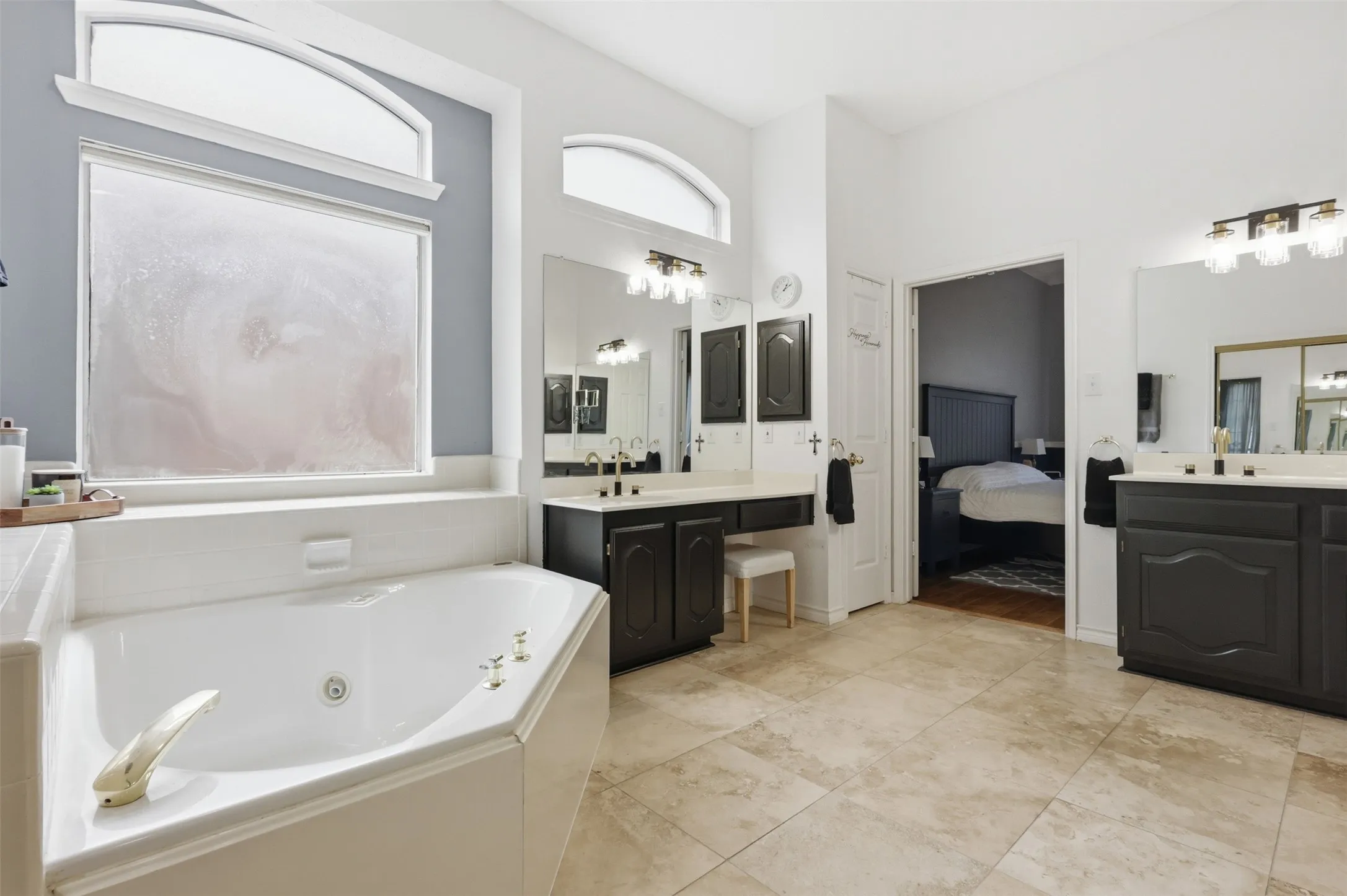 Spacious bathroom featuring a corner soaking tub, dual vanities with dark cabinetry, large mirrors, and tile flooring