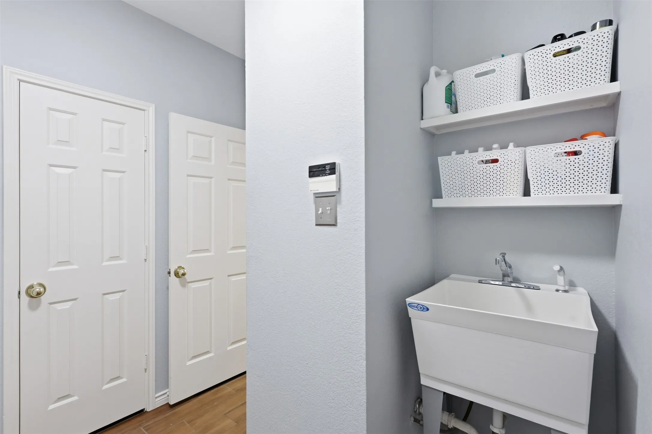 Utility sink with wall-mounted shelving, complemented by two white paneled doors and wood-finish flooring