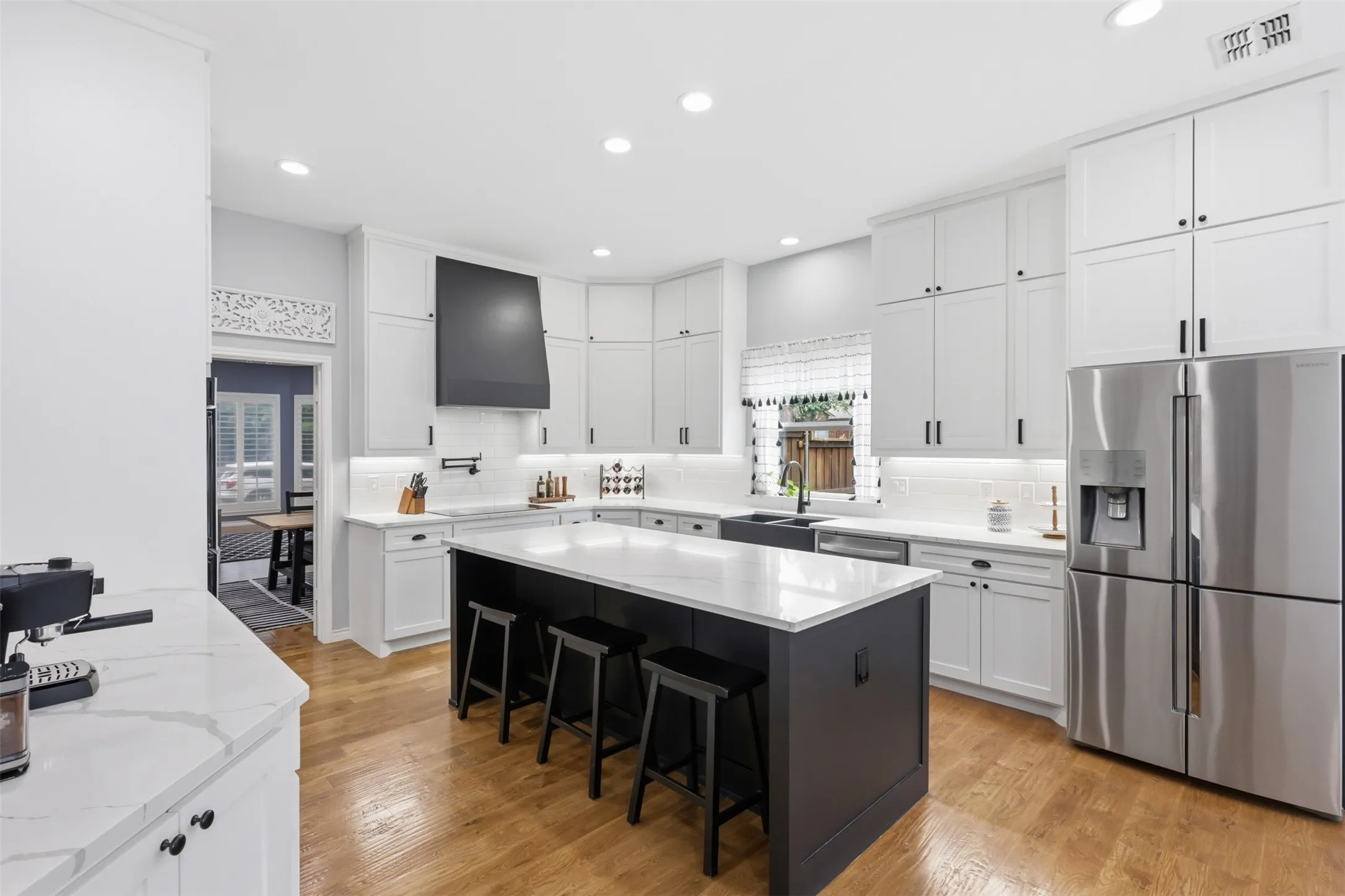 Gourmet kitchen featuring a large central island with seating, white shaker-style cabinetry, stainless steel appliances, white countertops, and wood-finish flooring