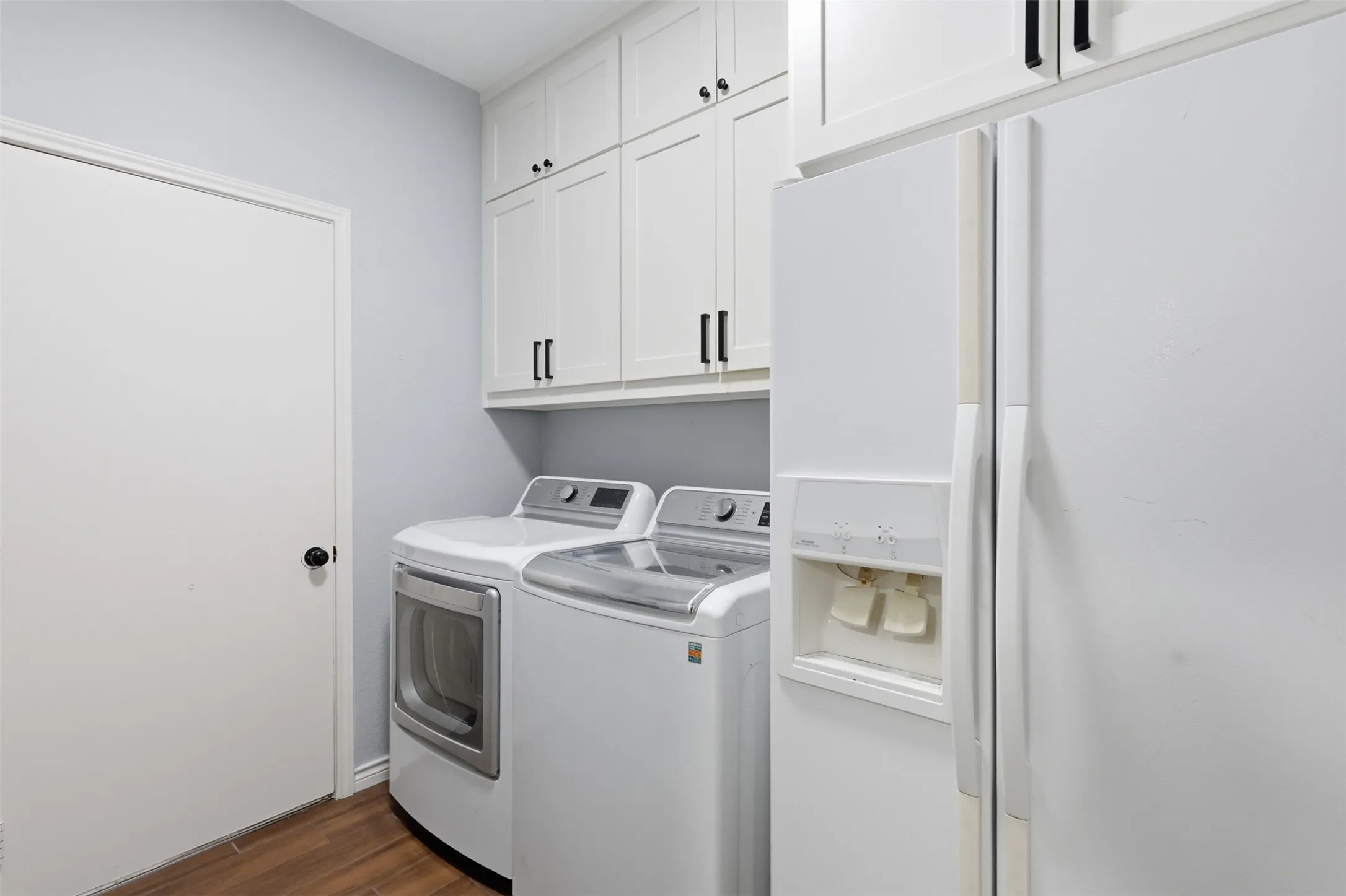 Laundry area featuring wood-finish flooring, white cabinetry with black hardware, and light gray wall paint