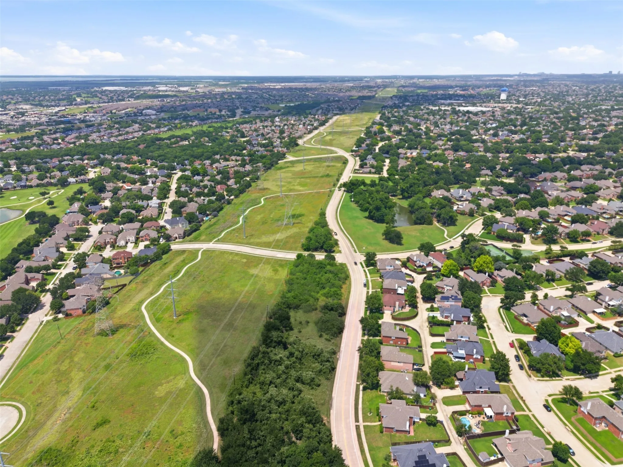 Expansive aerial capturing a suburban neighborhood with established homes, tree-lined streets, and extensive green spaces