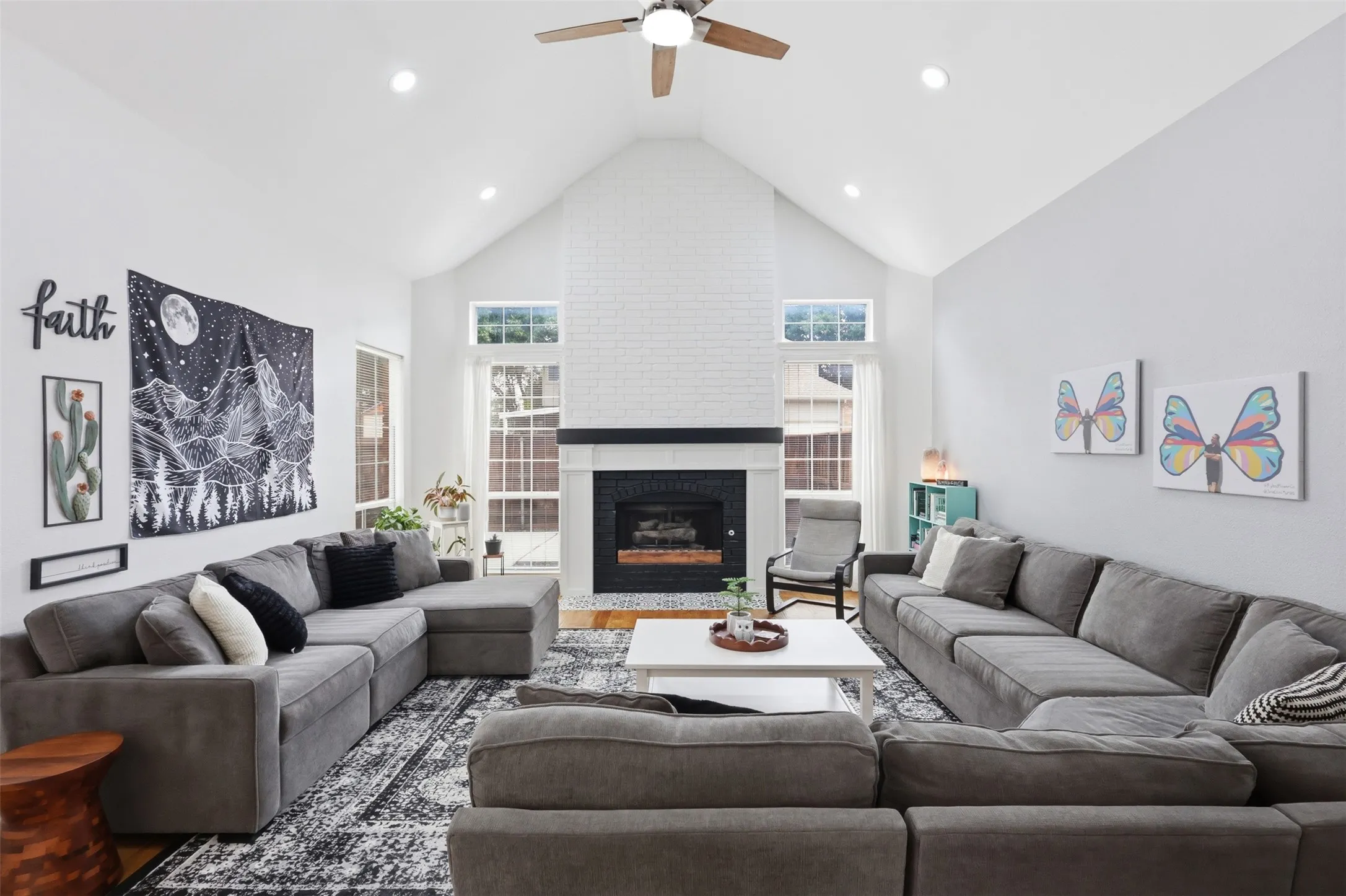 Vaulted ceiling living area featuring a white brick fireplace with a black mantel, recessed lighting, and a ceiling fan