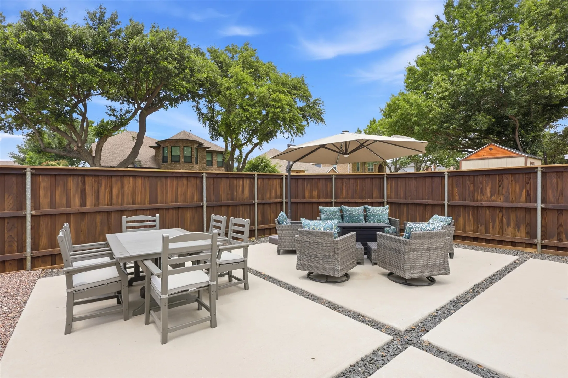 Private backyard featuring a concrete patio with gravel accents, a wooden privacy fence, and mature trees providing natural screening