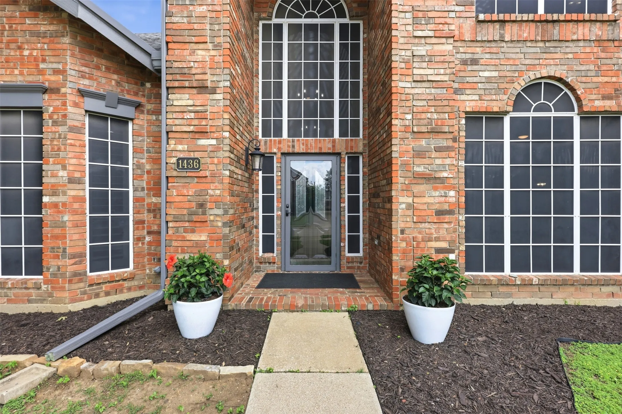 Brick facade home featuring a prominent arched transom window above the entry, a full-lite glass door, and a concrete walkway