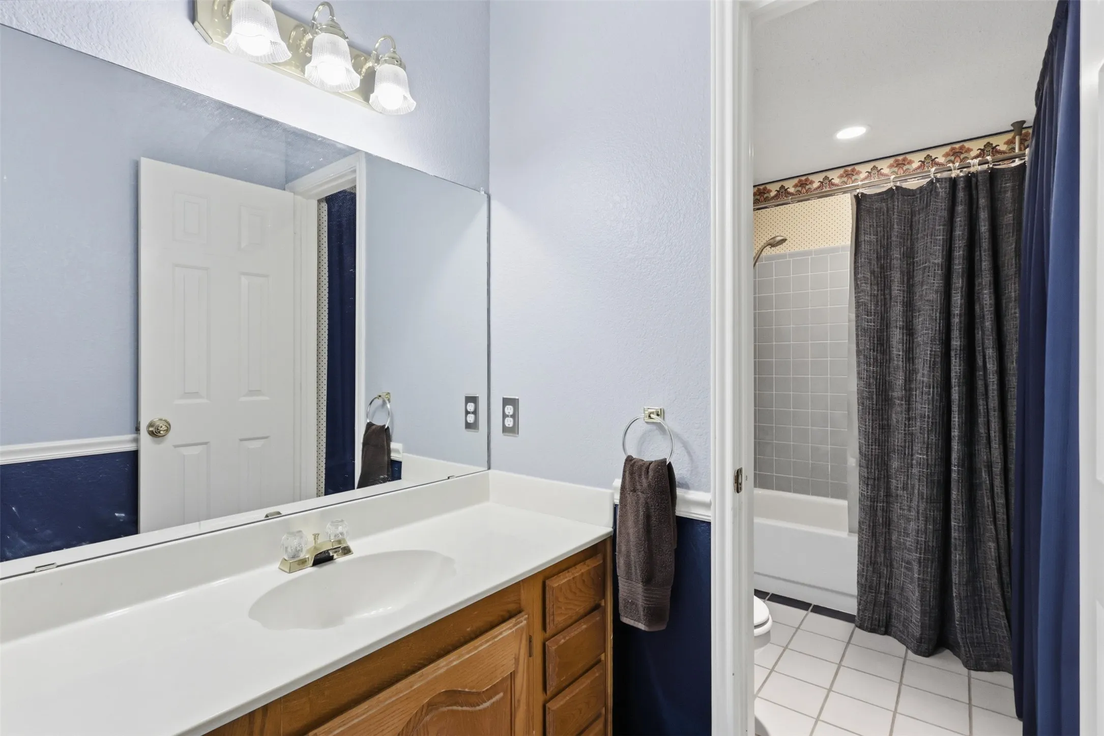 Bathroom vanity featuring a white countertop with an integrated sink, wood-finish cabinetry, and a full-width mirror