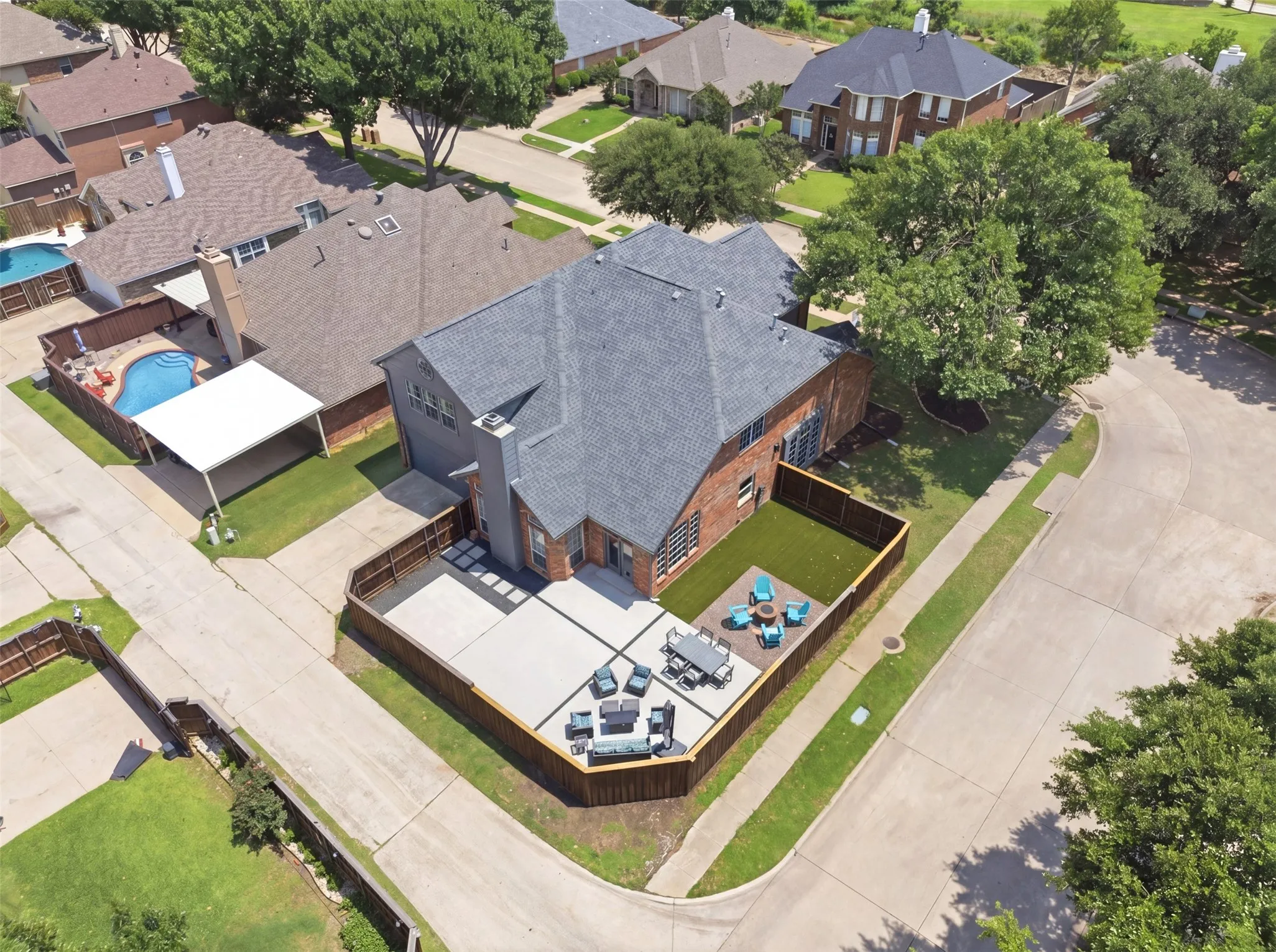 Residential property featuring a gray shingle roof, brick and stucco exterior, a fenced backyard with a patio, and artificial turf