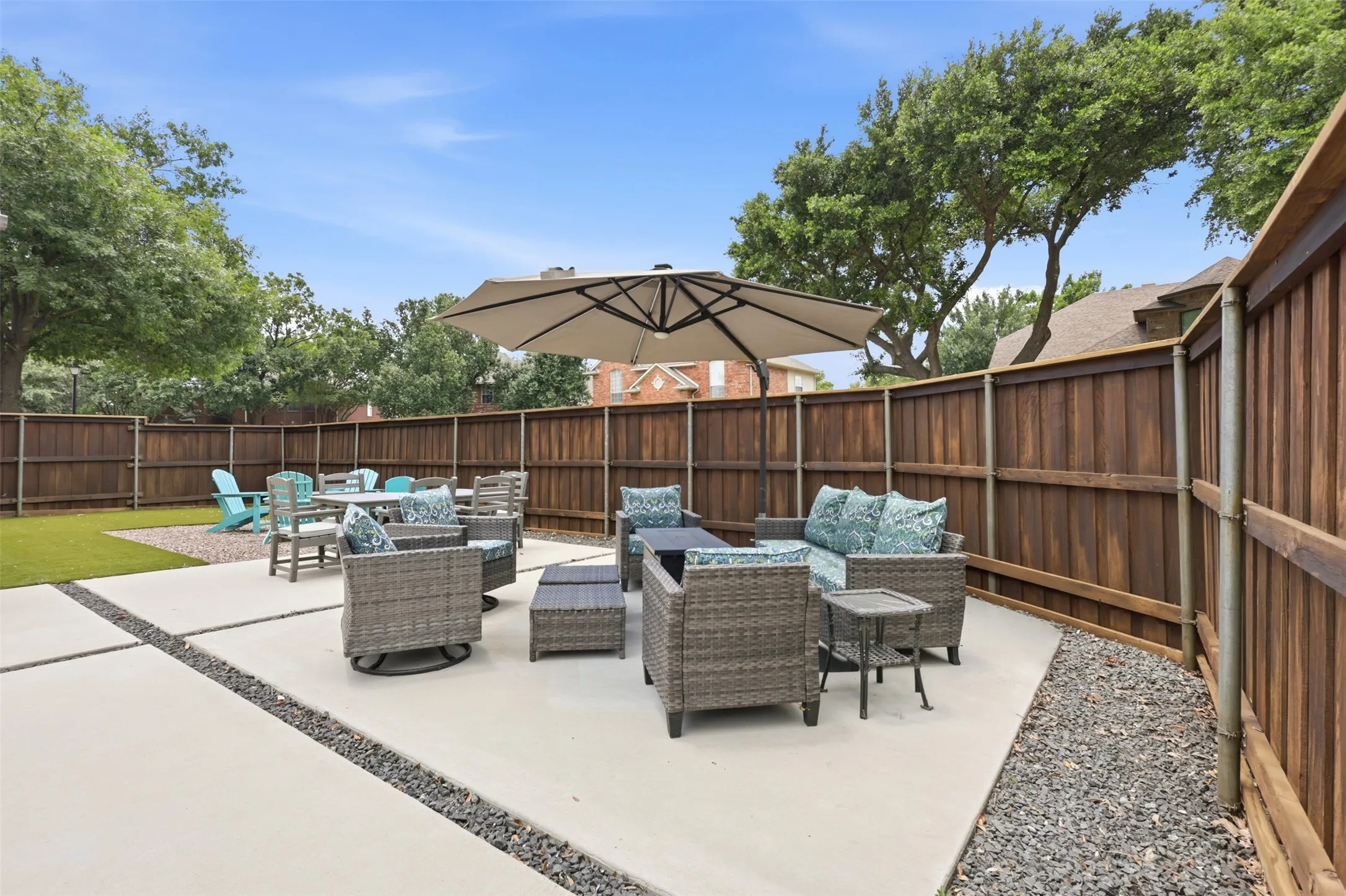 Expansive backyard featuring a concrete patio with gravel accents, artificial turf, and a wood privacy fence