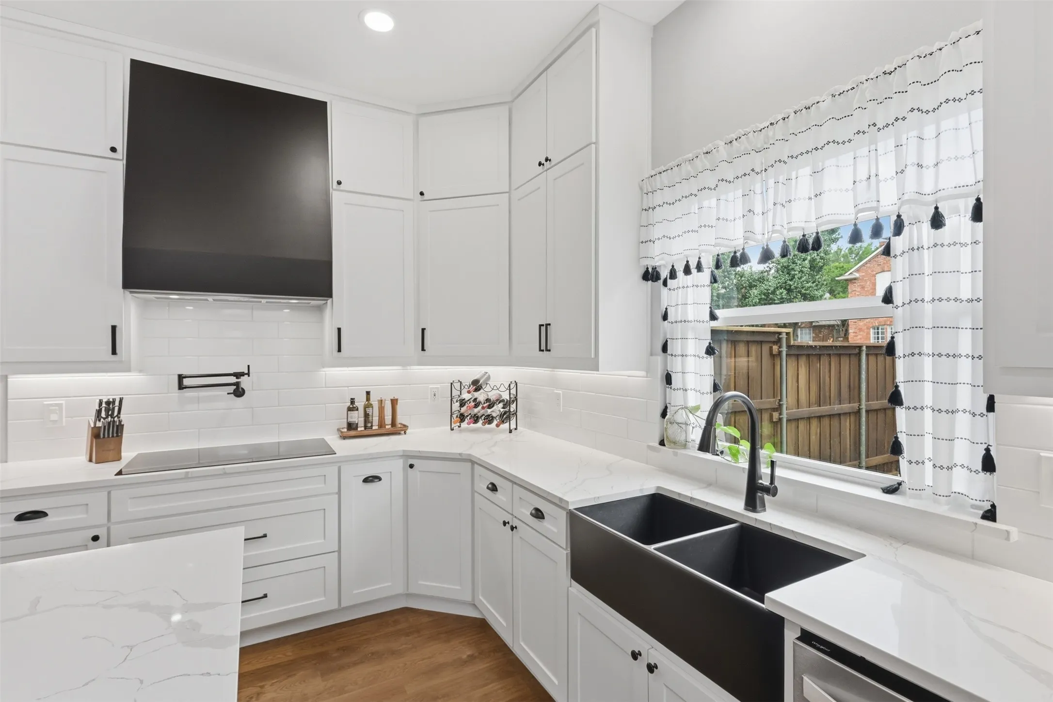 Bright kitchen featuring white shaker cabinetry, light countertops, subway tile backsplash, a black farmhouse-style sink, and stainless steel appliances