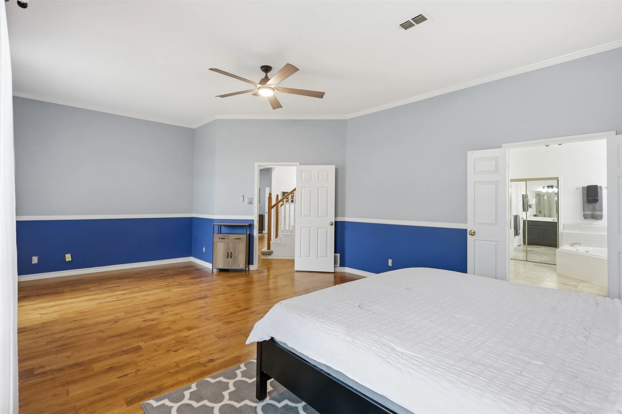 Spacious bedroom featuring wood-finish flooring, a ceiling fan, and crown molding