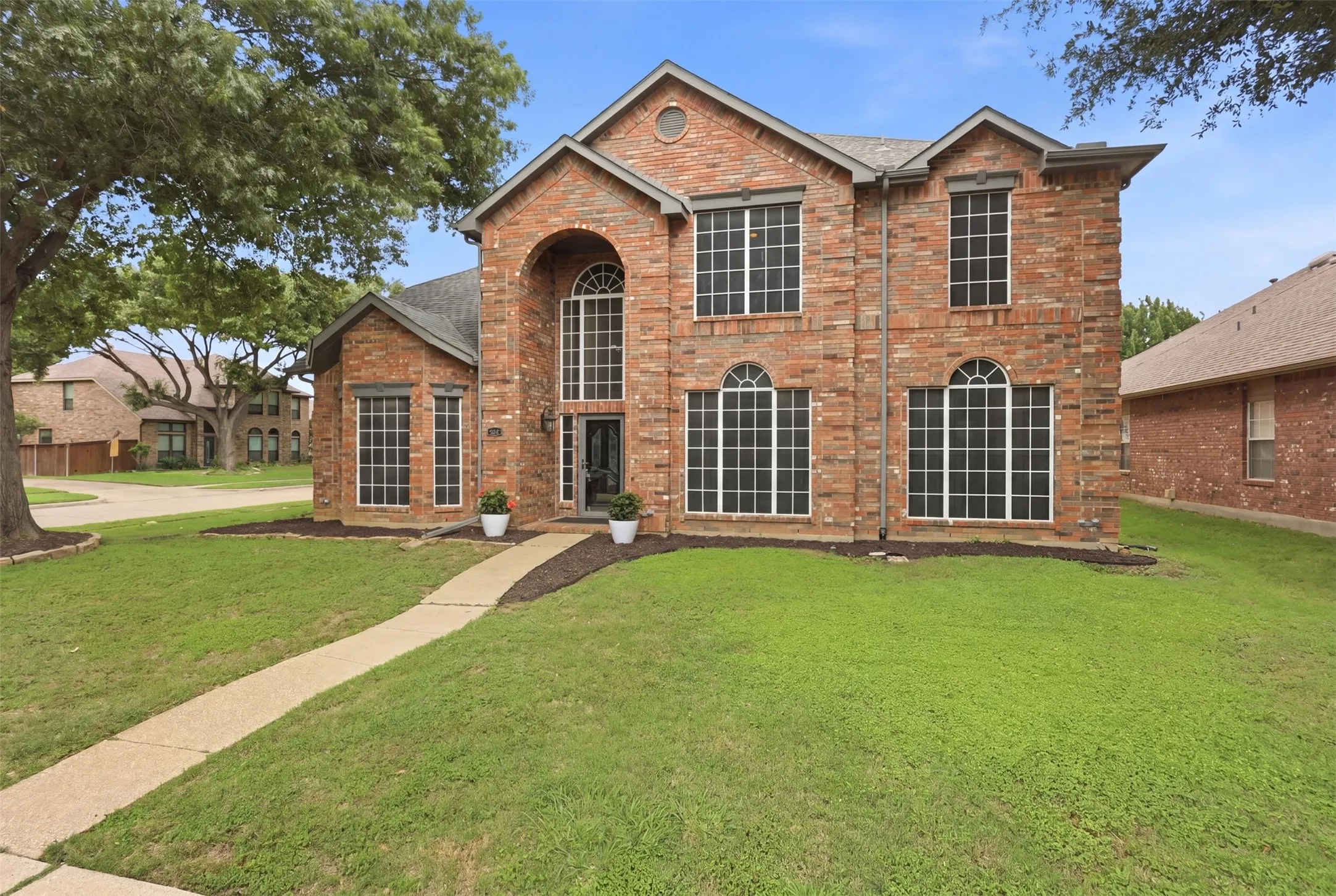 Brick exterior with a prominent arched entry, multiple large windows, a paved walkway, and mature trees