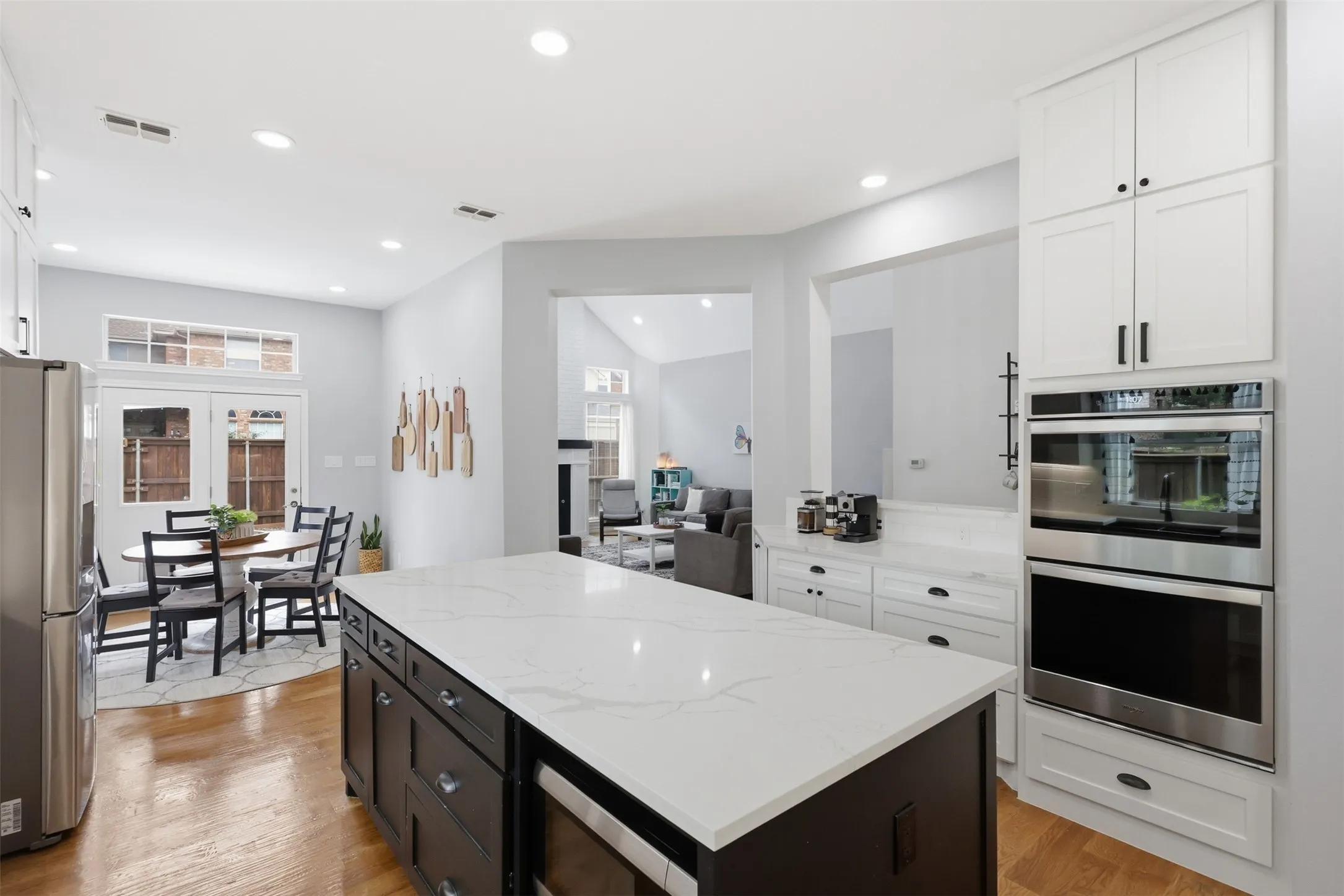 Kitchen featuring a large island with a quartz countertop, stainless steel appliances, recessed lighting, white shaker-style cabinetry, and wood-finish flooring