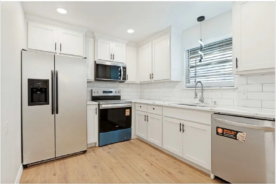 Kitchen featuring white shaker cabinetry with matte black hardware, stainless steel appliances, light-toned wood-finish flooring, white subway tile backsplash, and light-toned countertops