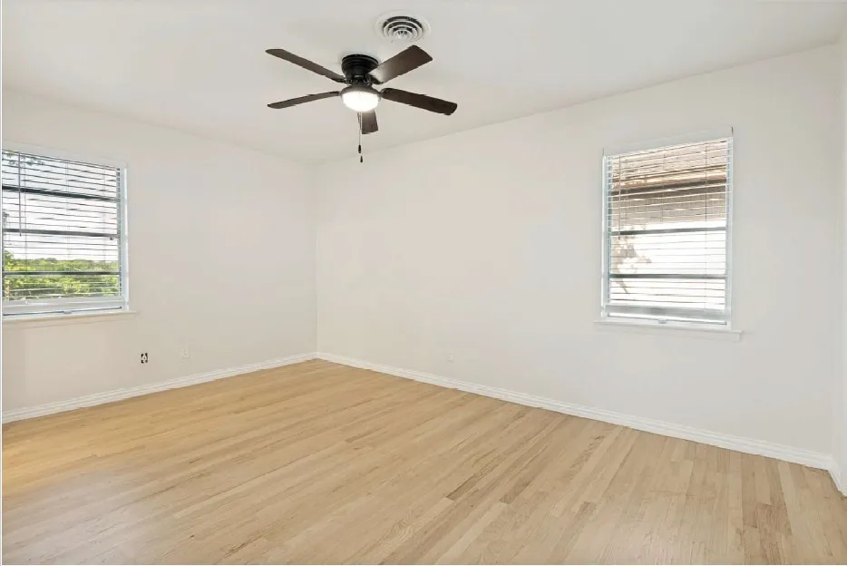 Room featuring light wood-finish flooring, two windows with blinds, a ceiling fan with integrated lighting, and white walls