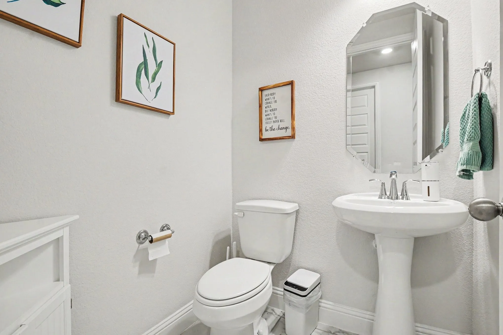 Pedestal sink with chrome faucet, complemented by a decorative octagonal mirror