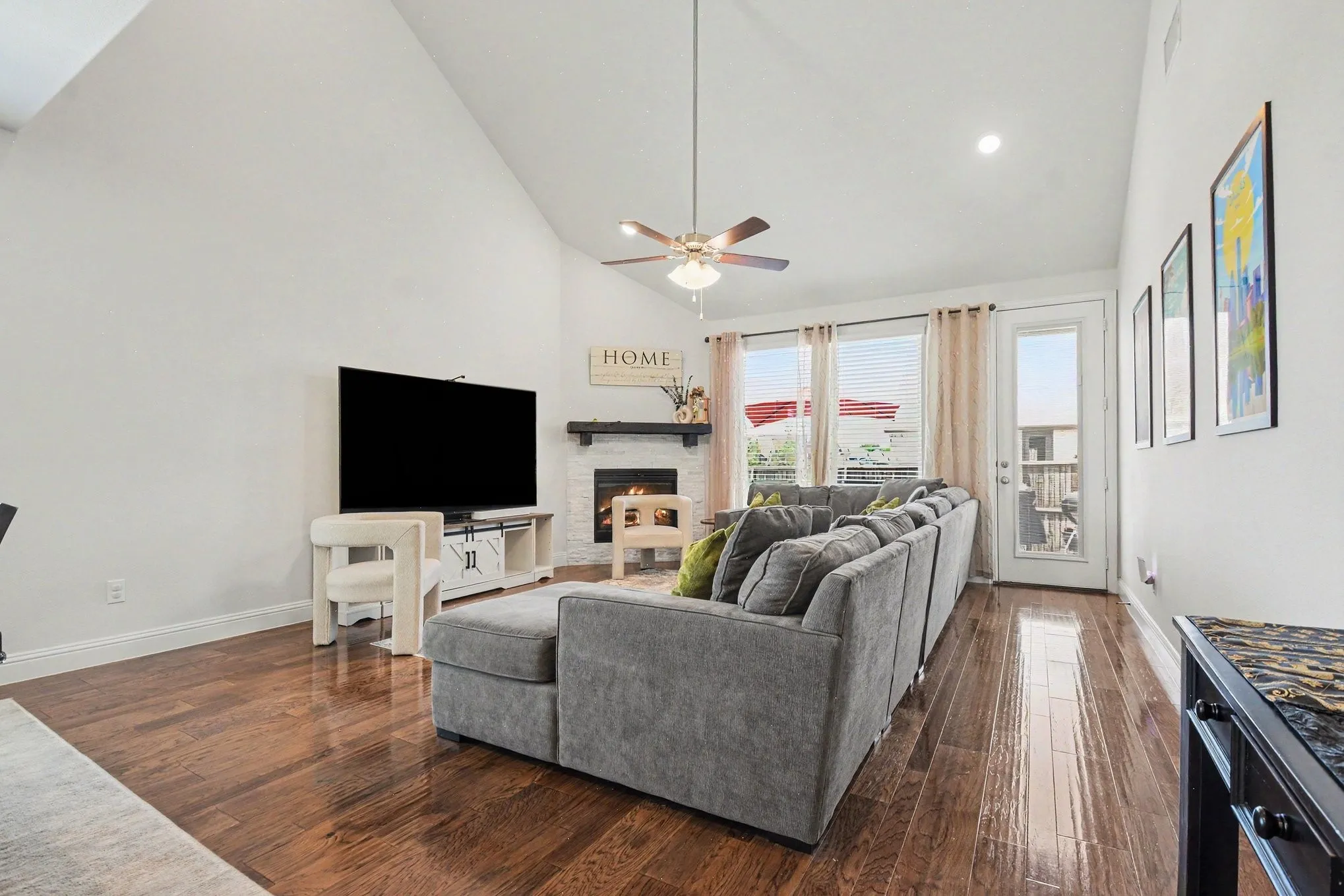 Living area featuring wood-finish flooring, a vaulted ceiling, and a ceiling fan with integrated lighting